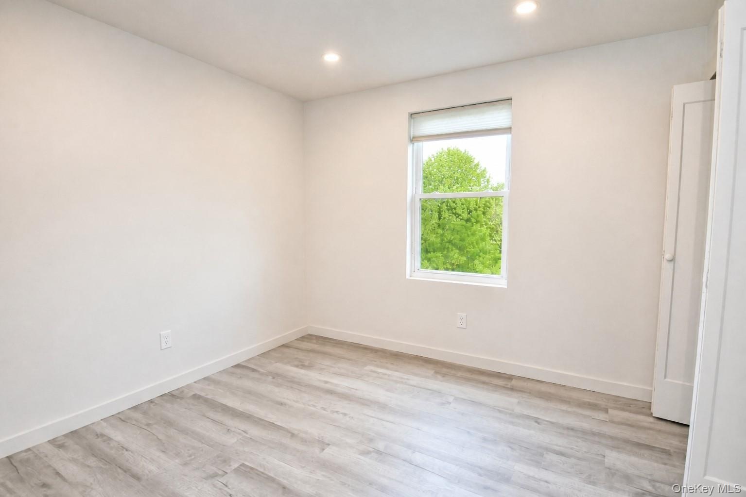 Bedroom with a window, recessed lighting and wood-look plank flooring.