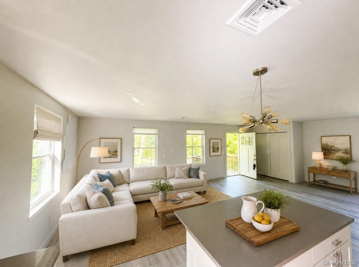 Virtually staged. Living room with three windows and chandelier, viewed from the kitchen island.