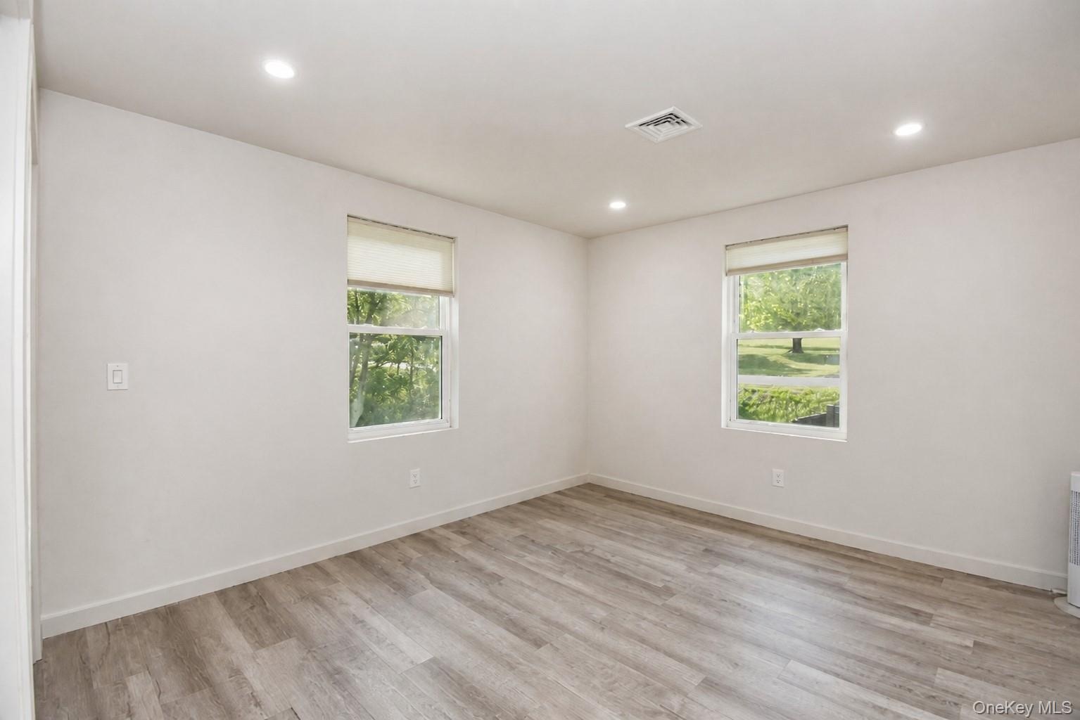 Bedroom with two windows, recessed lighting and wood-look plank flooring.