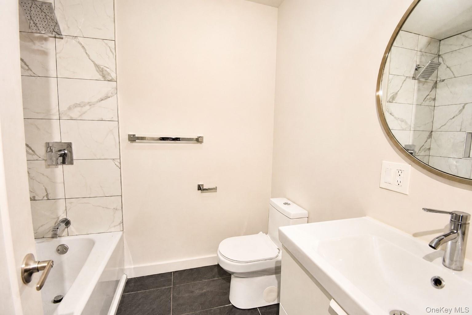 Full bathroom with tub/shower, tiled surround, floating vanity, round mirror and tile floor.