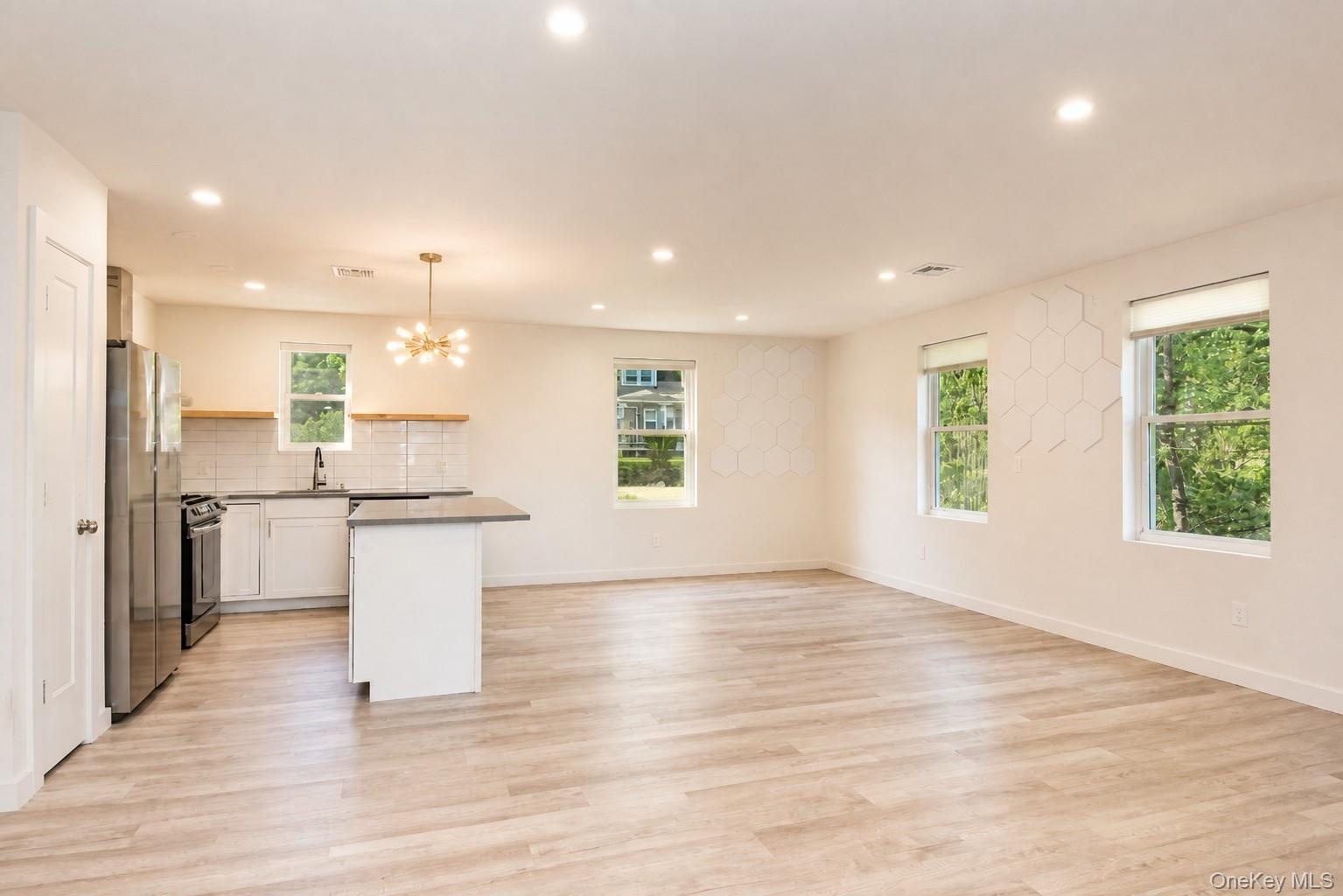 Living and dining area viewed from the kitchen, with windows on two walls and wood-look flooring.