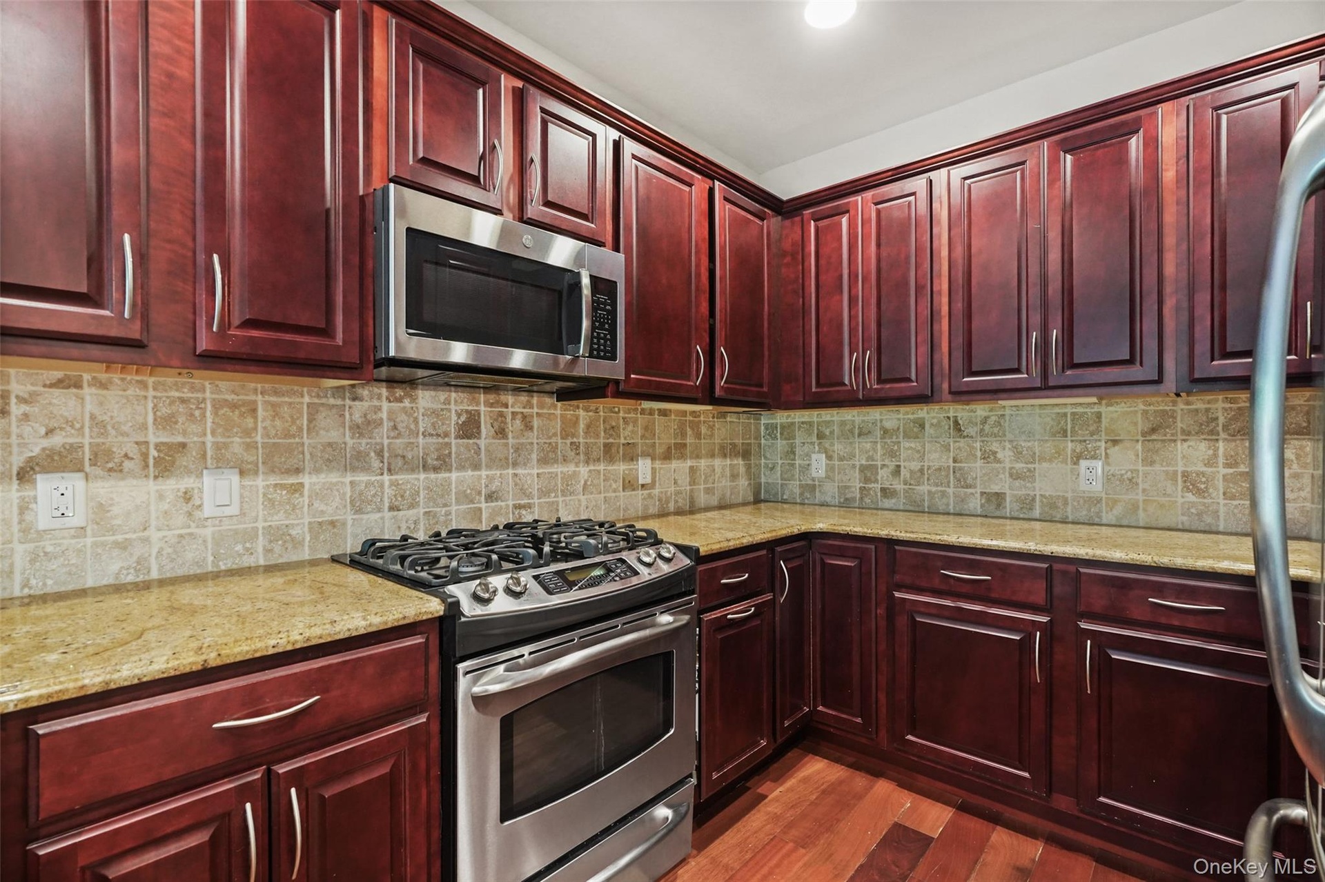 Cherry wood cabinetry, stainless steel range, stainless steel microwave, stone countertops, and a tile backsplash
