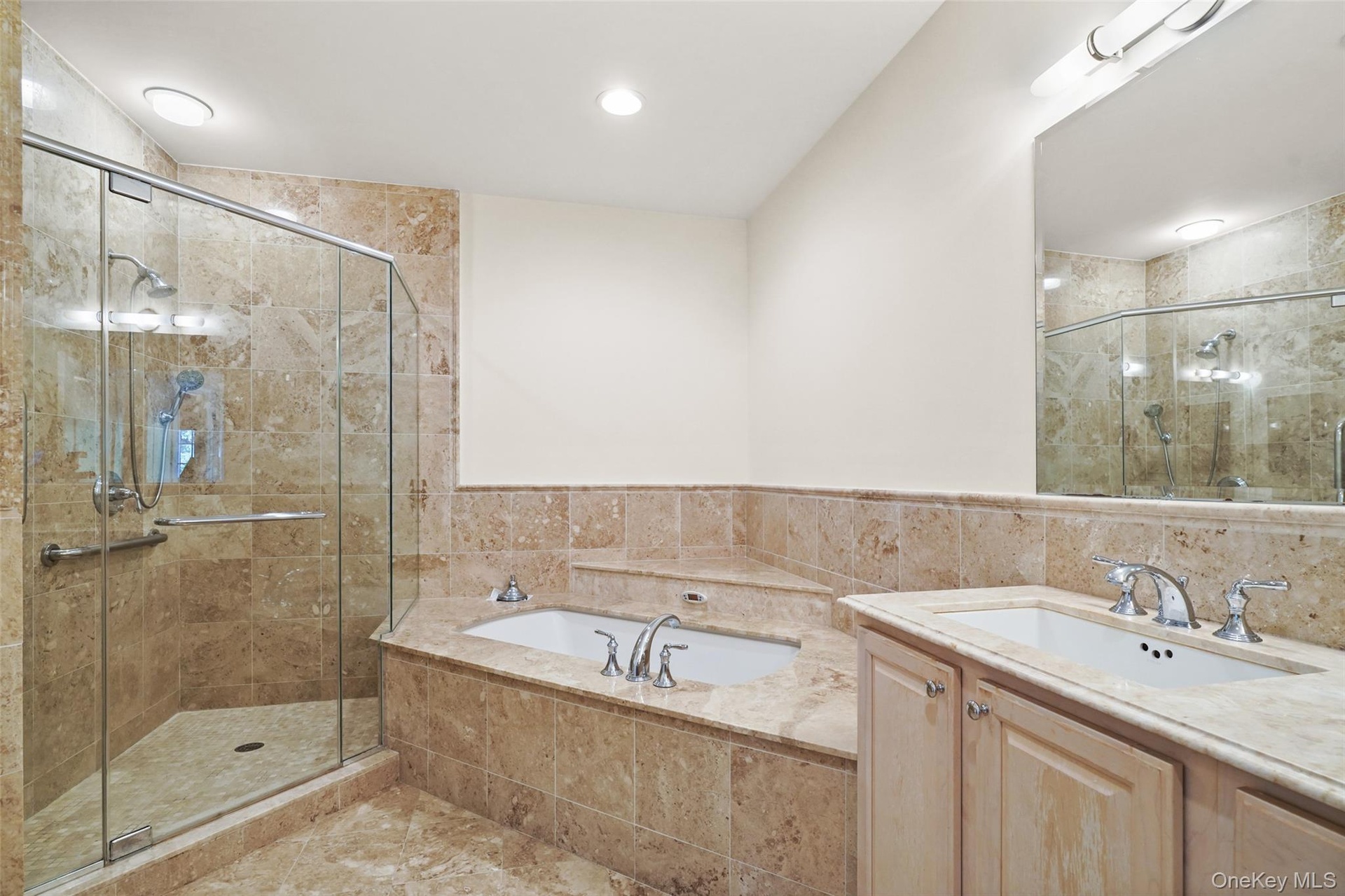 Glass-enclosed shower with a handheld shower fixture, built-in bathtub, single vanity with light wood cabinetry, and a full-width mirror