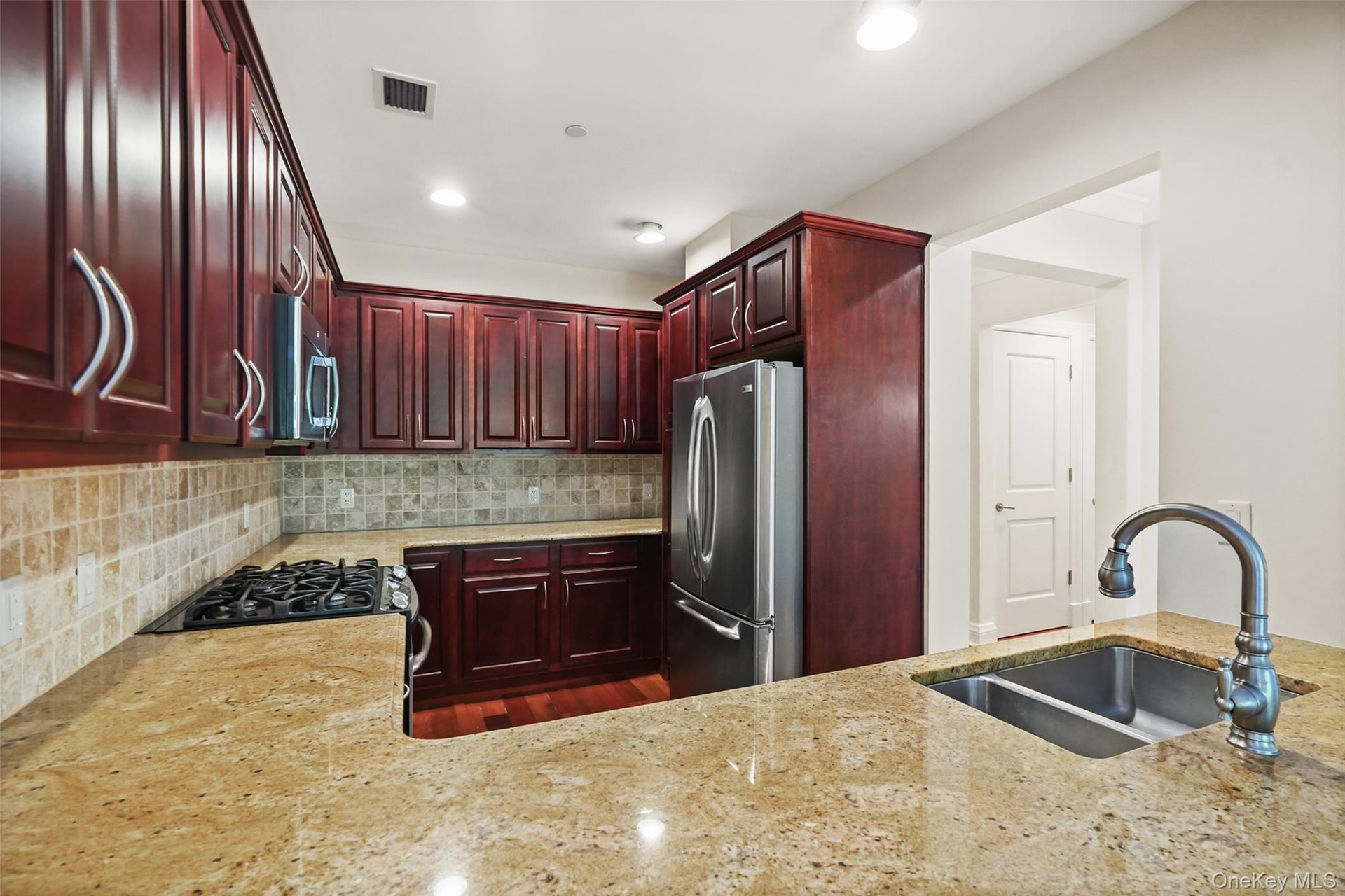 Rich wood-finish cabinetry with curved pulls, stainless steel appliances, speckled stone countertops, and a tile backsplash