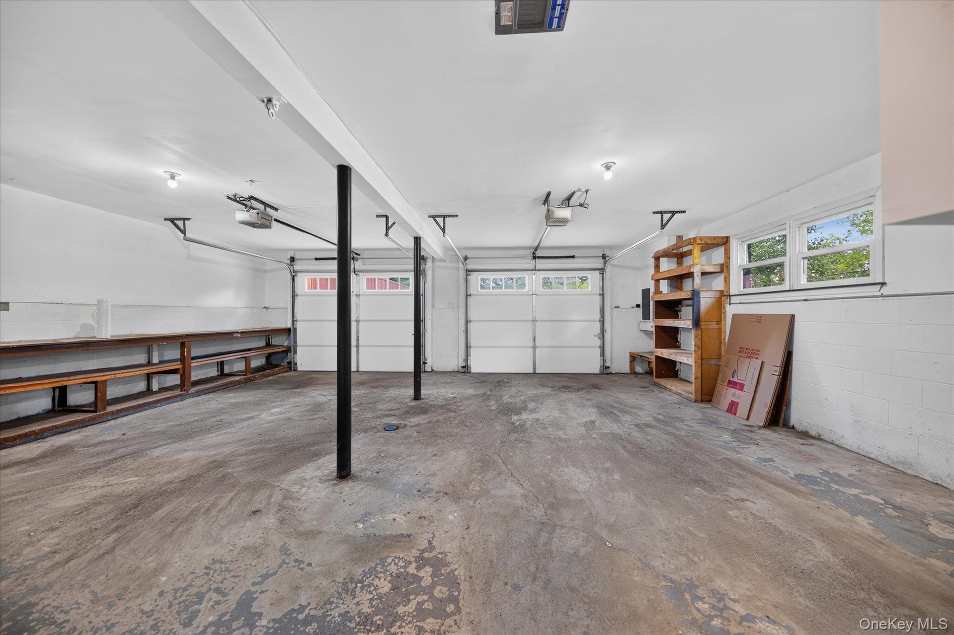 Expansive garage with concrete flooring, dual garage doors, built-in shelving, and transom windows