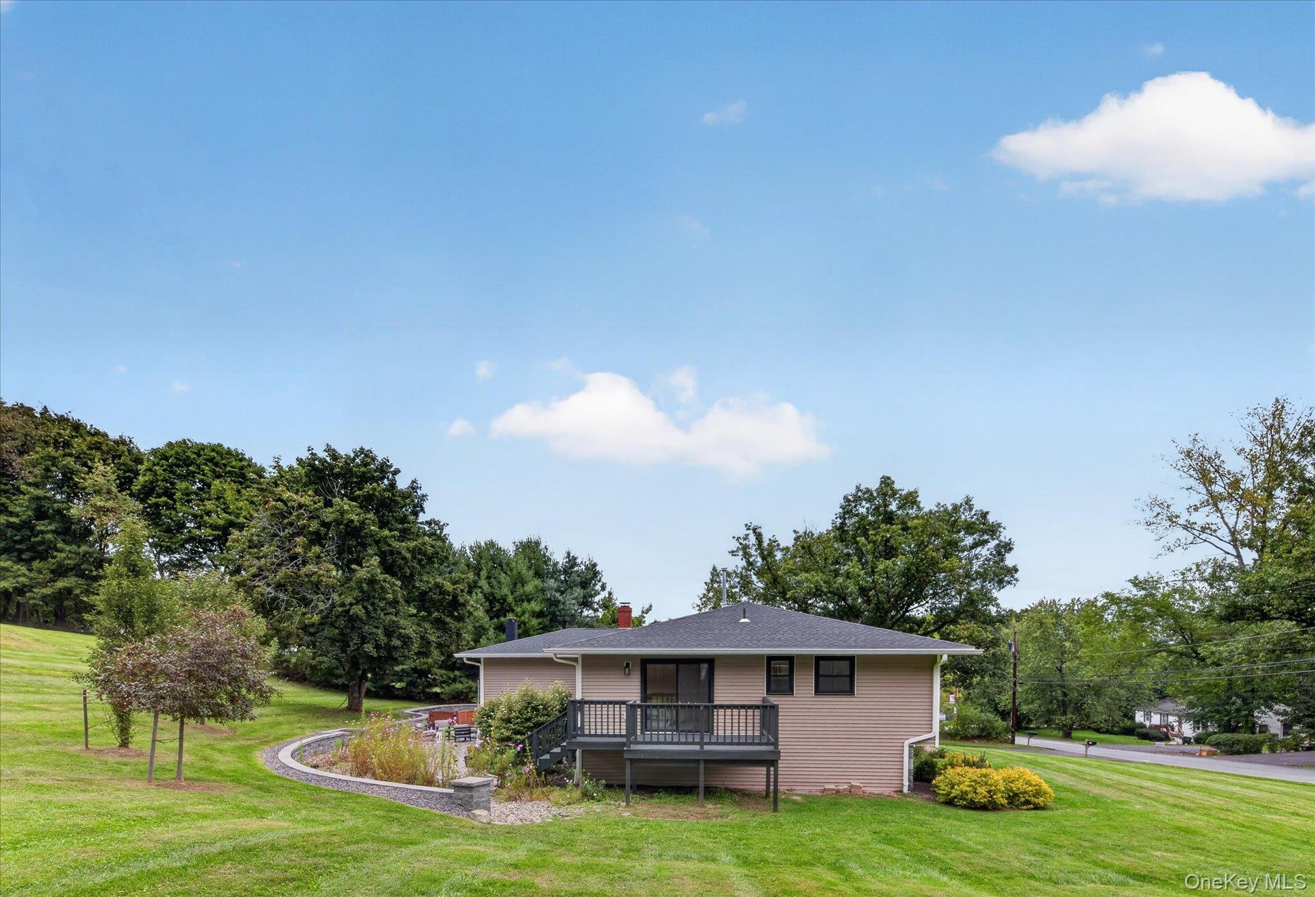 Expansive green lawn, multi-level composite deck, stone retaining wall, mature trees, and a paved street
