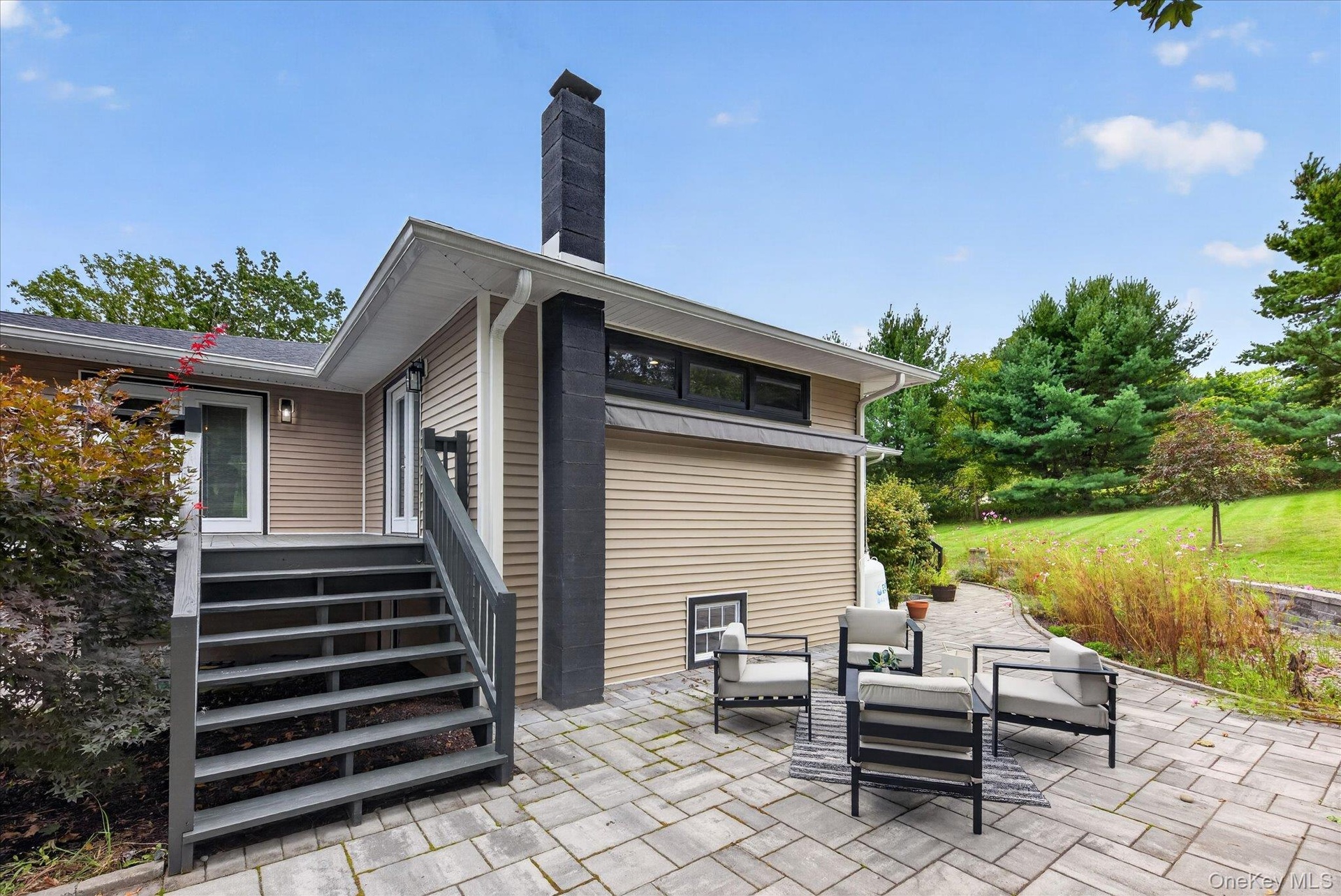 Exterior featuring siding, multiple windows, a prominent black chimney, and a stone paver patio