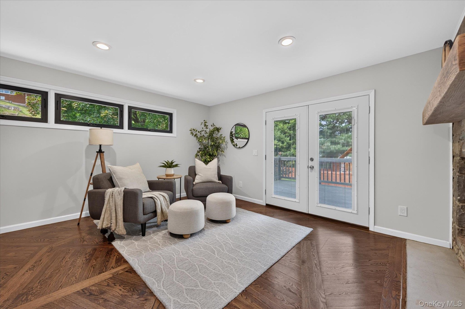 Hardwood flooring with a geometric pattern, white double doors with glass panes, recessed lighting, and a stone-faced fireplace with a wood mantle