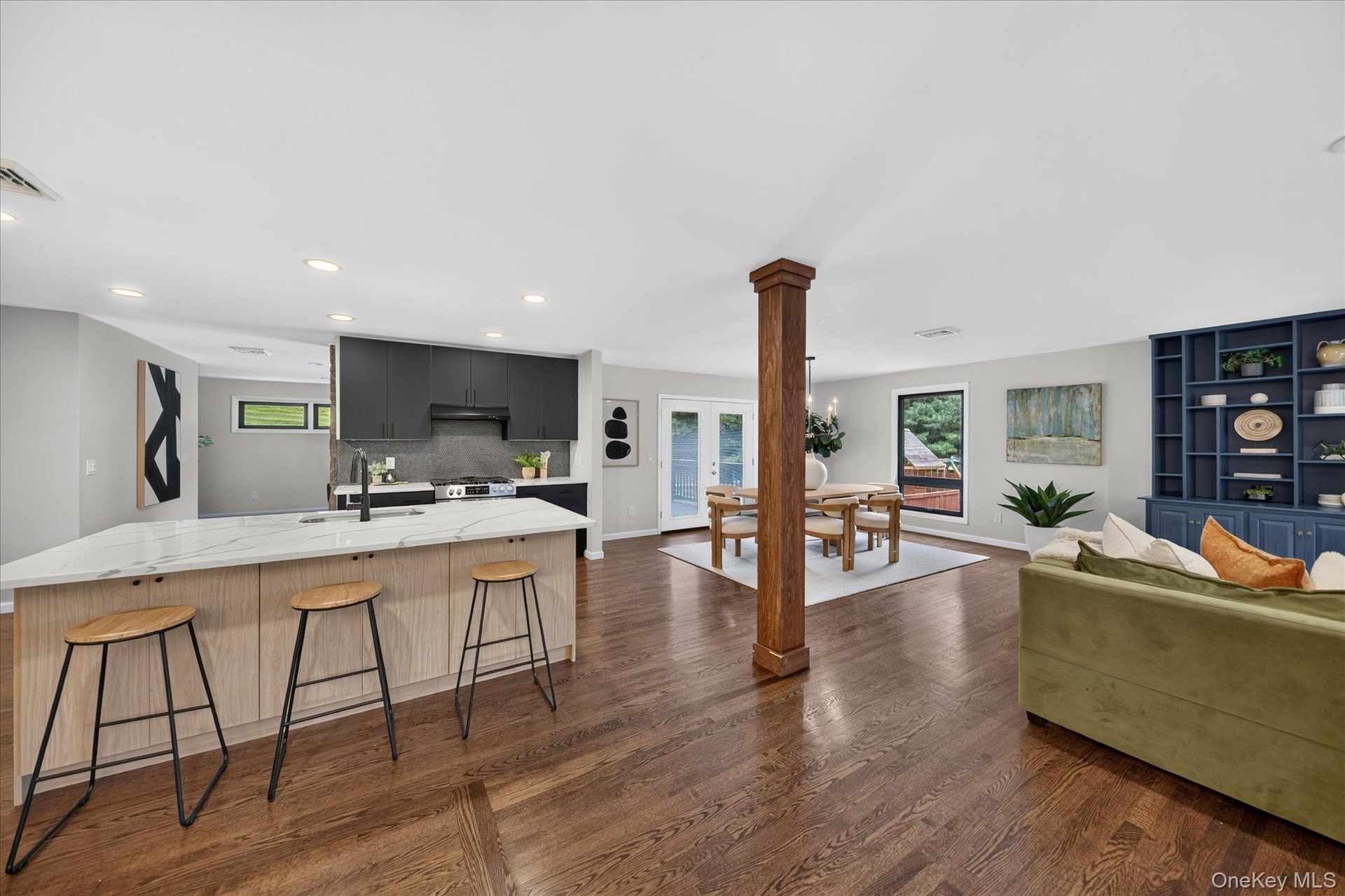 Kitchen island with marble-look countertop and integrated sink, dark wood-finish flooring, built-in shelving unit, black cabinetry, and French doors