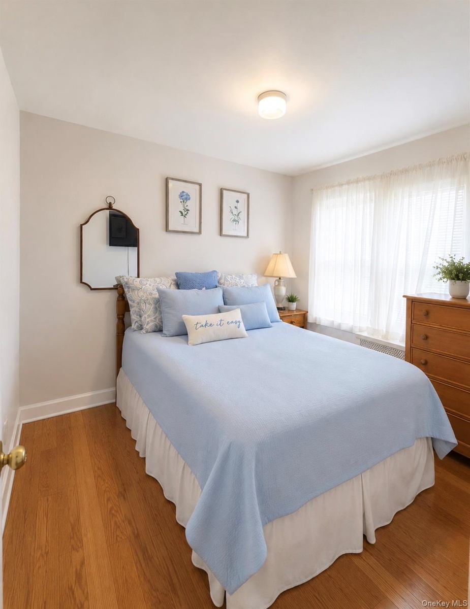 Bedroom featuring wood-finish flooring, a flush-mount ceiling light fixture, and a window with sheer curtains
