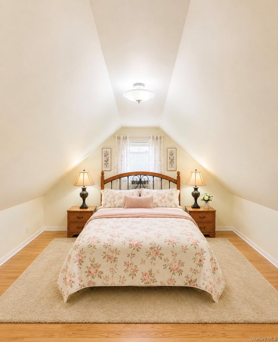 Attic bedroom featuring pitched ceilings, wood-finish flooring, and a window with sheer curtains