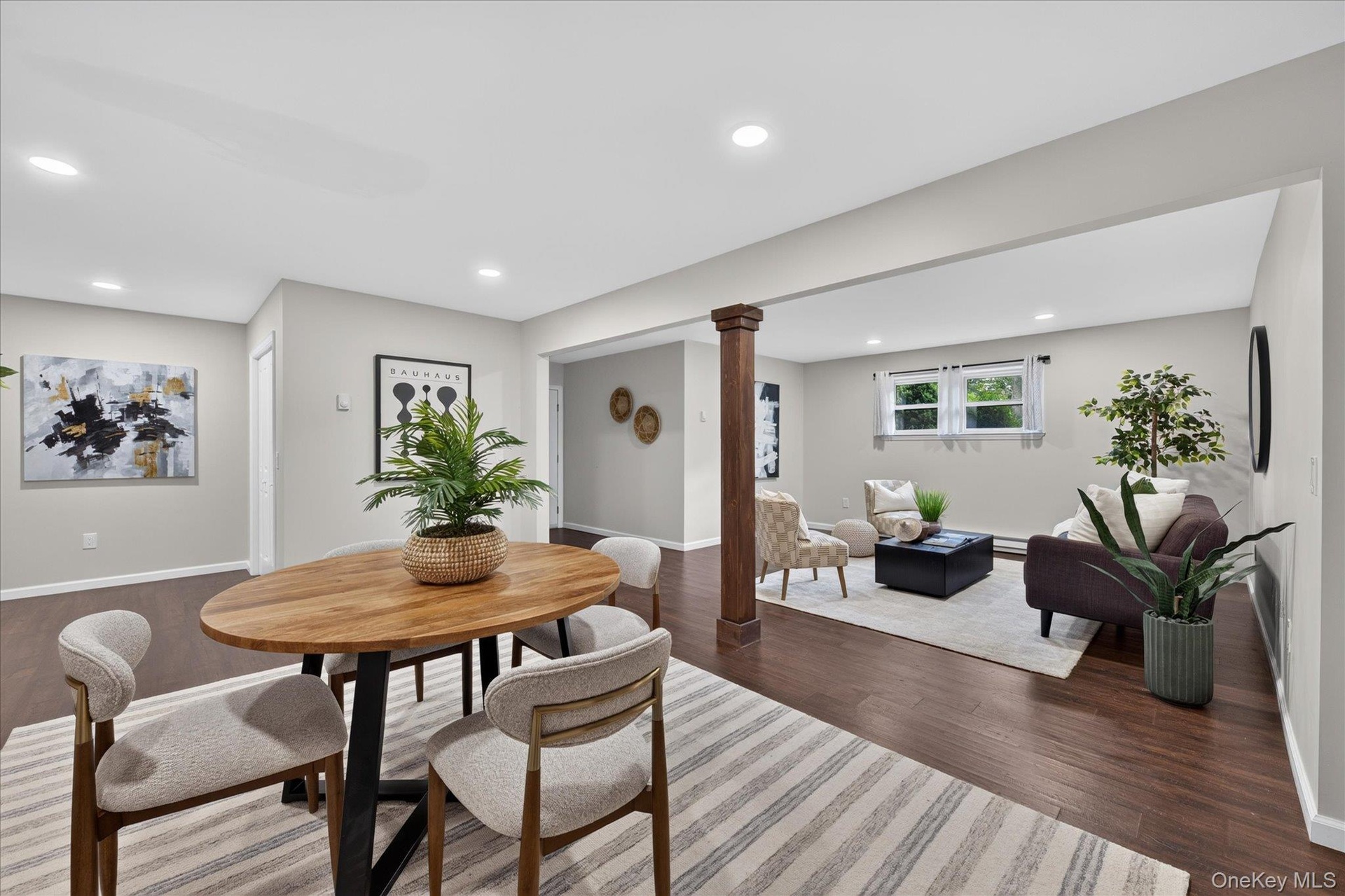 Recessed lighting, wood-finish flooring, light grey wall paint, white trim, and a wood-wrapped column