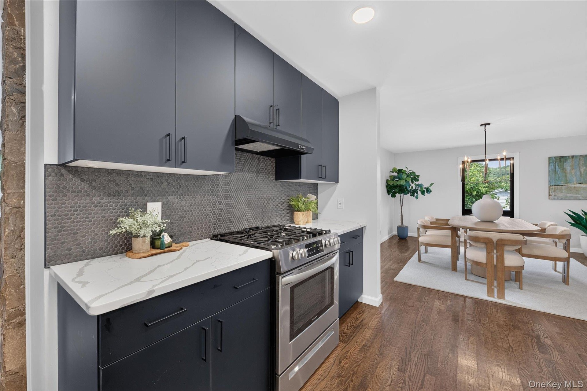 Matte navy cabinetry, white countertops with veining, stainless steel range, gray mosaic tile backsplash, and wood-finish flooring