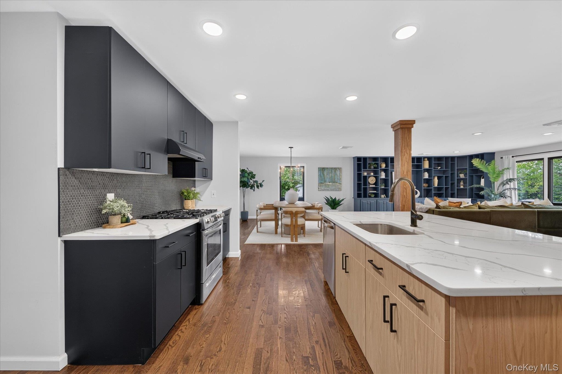 Modern kitchen featuring a large island with an undermount sink, stainless steel appliances, dark cabinetry, and wood-finish flooring