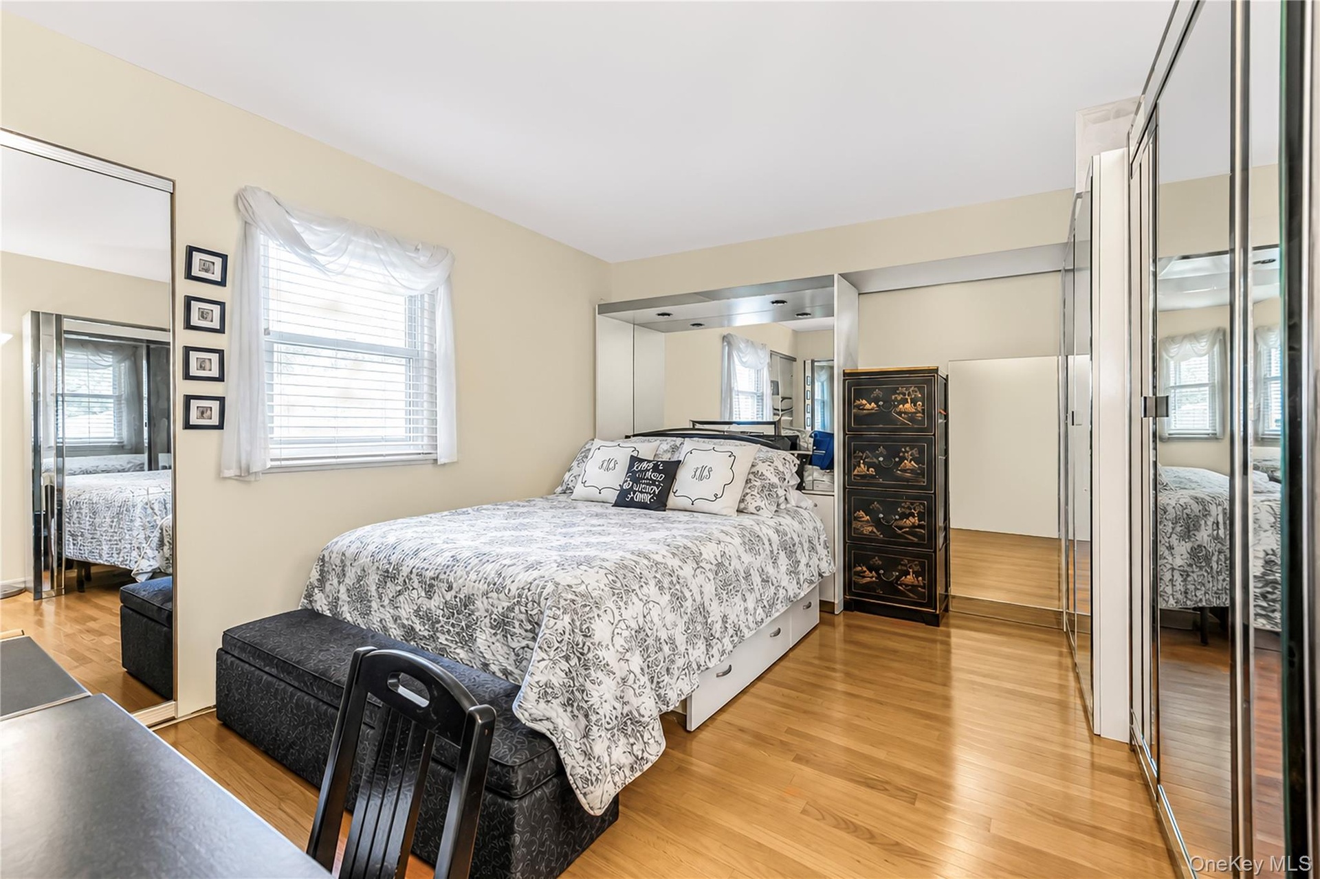 Hardwood flooring, mirrored closet doors, a built-in mirrored headboard, and a window with blinds