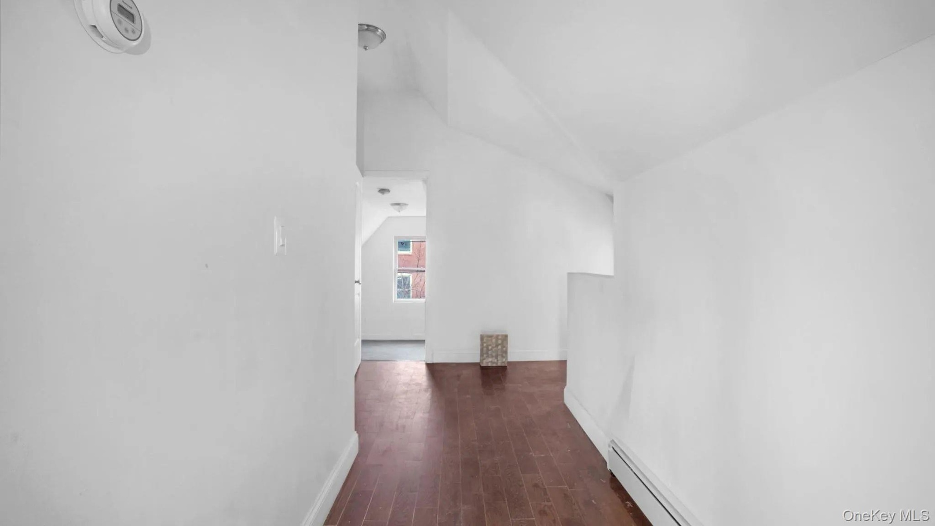 Hall featuring dark wood-type flooring, a baseboard radiator, and vaulted ceiling