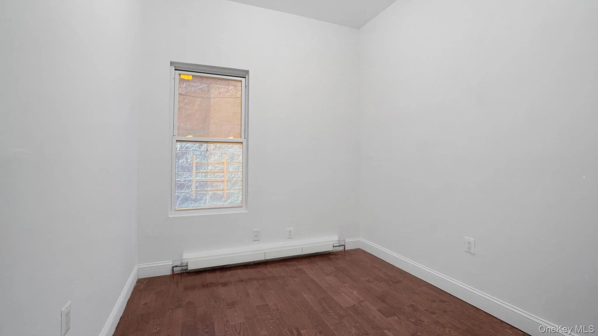Spare room featuring a baseboard heating unit and dark hardwood / wood-style flooring