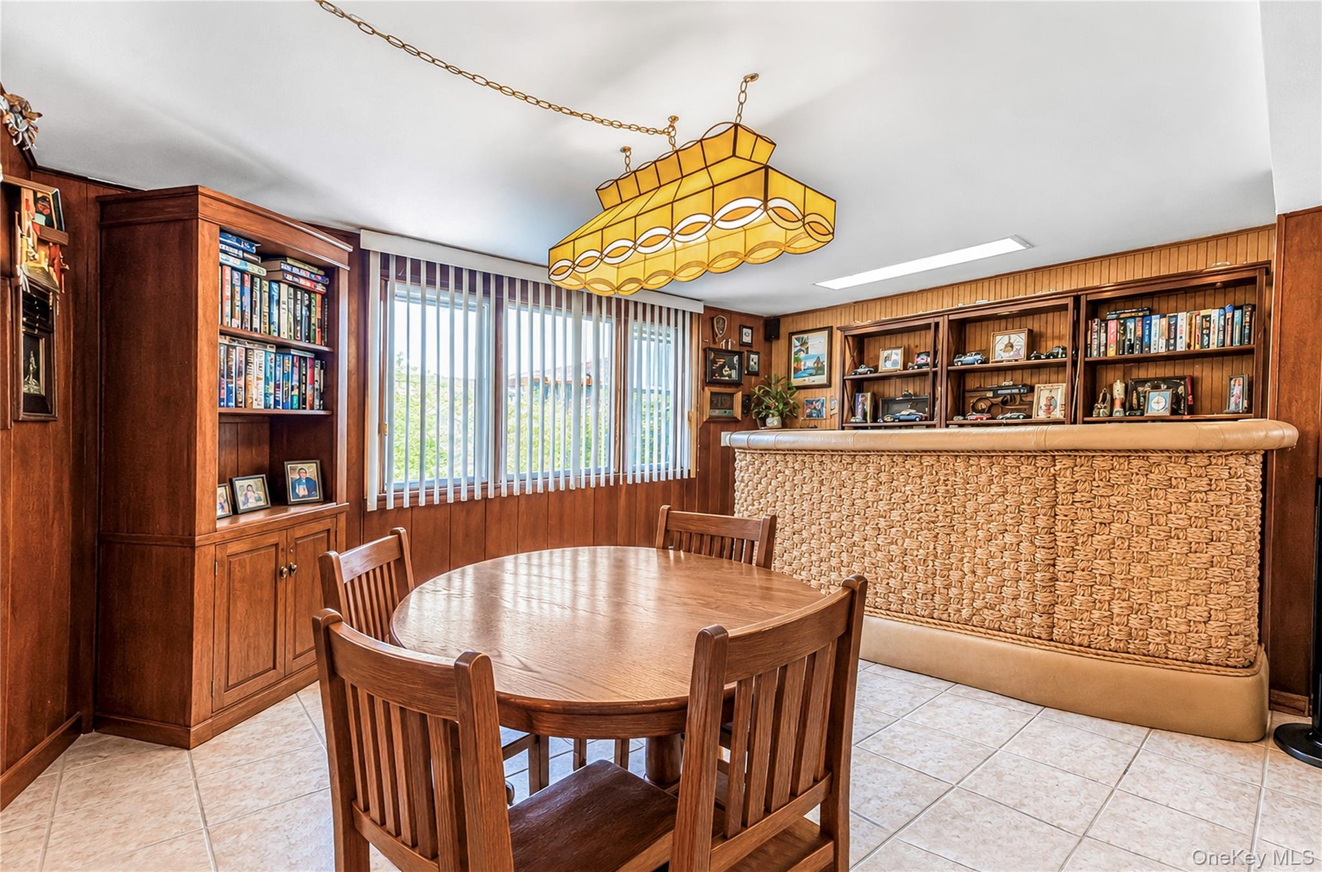 Wood-paneled room featuring extensive built-in shelving, a patterned bar with a built-in display, and tiled flooring