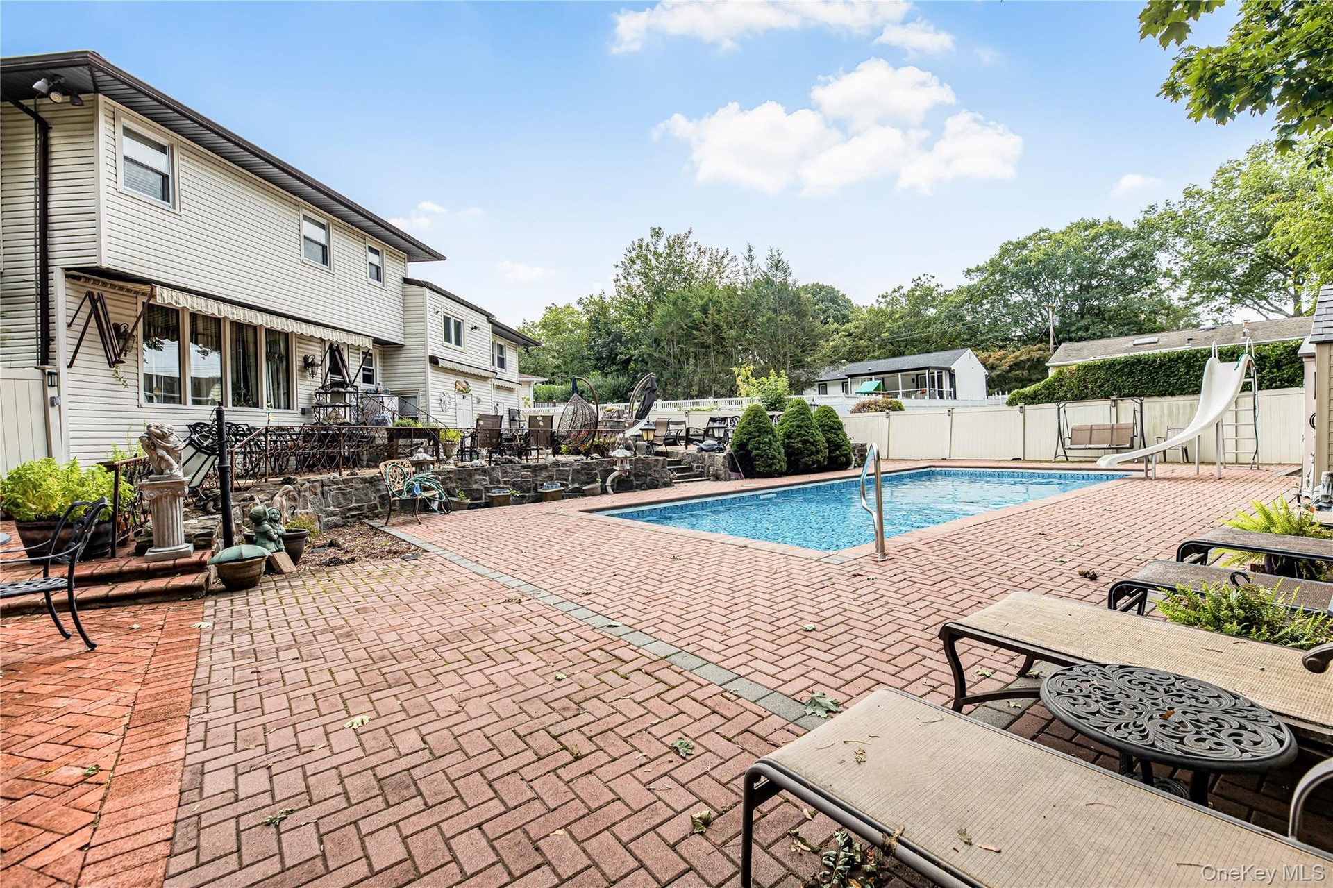 Swimming pool with a water slide, surrounded by a brick paver patio and privacy fencing