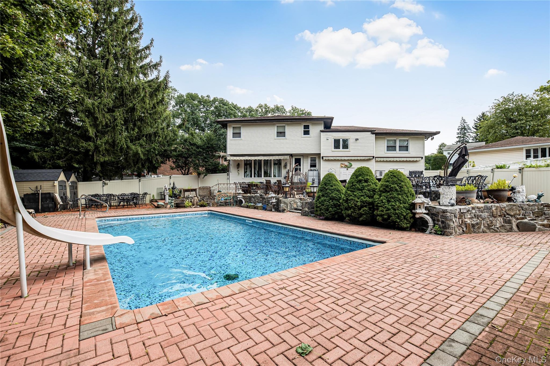 Swimming pool with a water slide, surrounded by a brick paver patio and privacy fencing