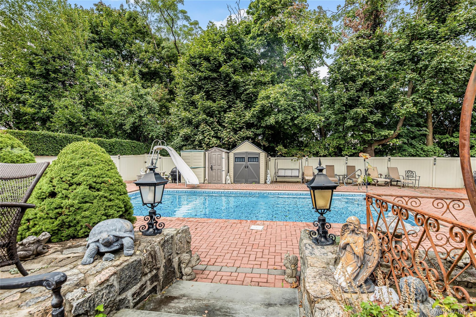 Swimming pool with a water slide, surrounded by a brick paver patio and privacy fencing