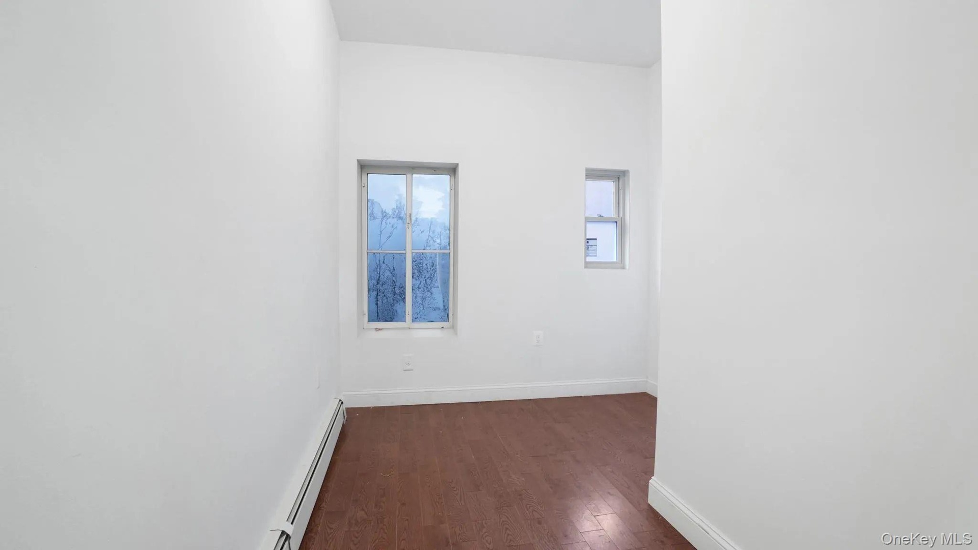 Empty room with a baseboard heating unit and dark hardwood / wood-style flooring