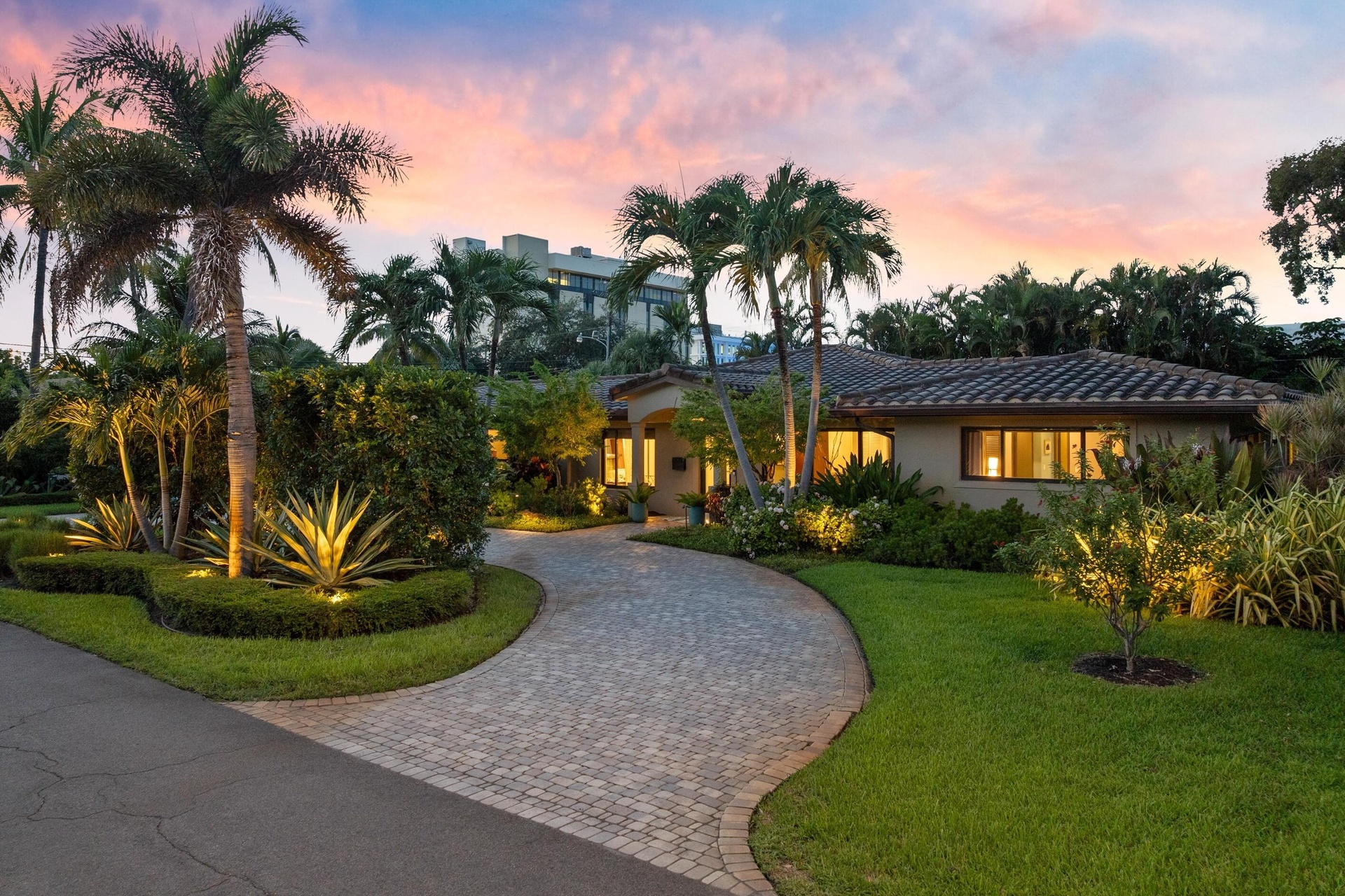 Paver driveway, lush landscaping, mature palm trees, exterior lighting, and a tile roof