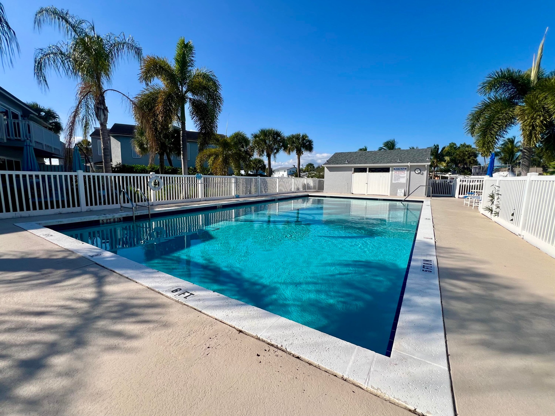 Expansive outdoor swimming pool with a surrounding white picket fence, concrete decking, and tropical landscaping