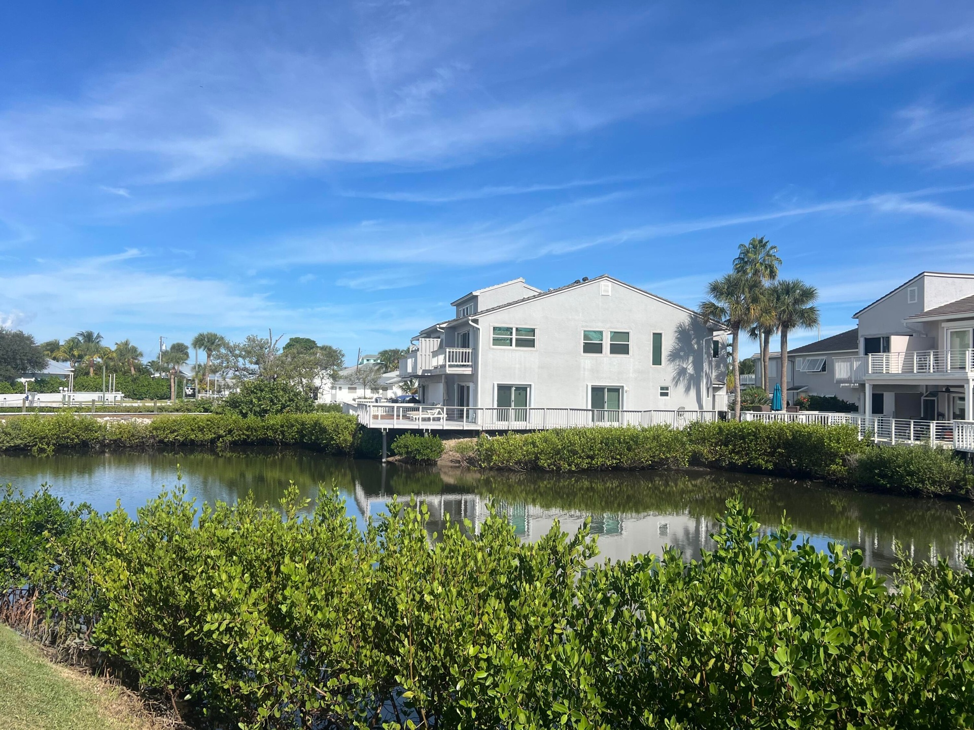 Waterfront property featuring multiple balconies, a white exterior, and mature palm trees