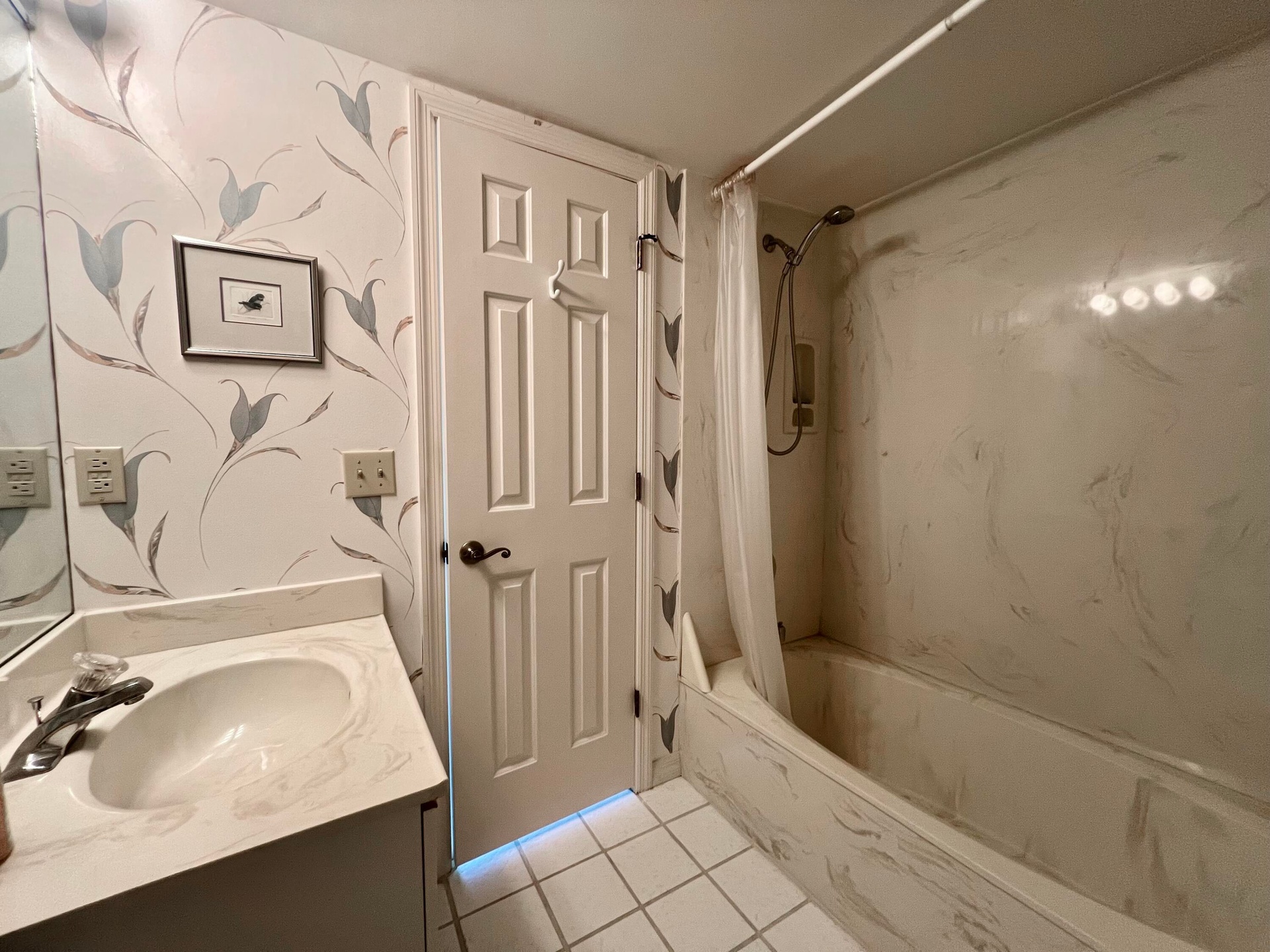 Vanity with integrated sink and countertop, textured wallpaper, tile flooring, built-in bathtub with shower, and multi-panel door