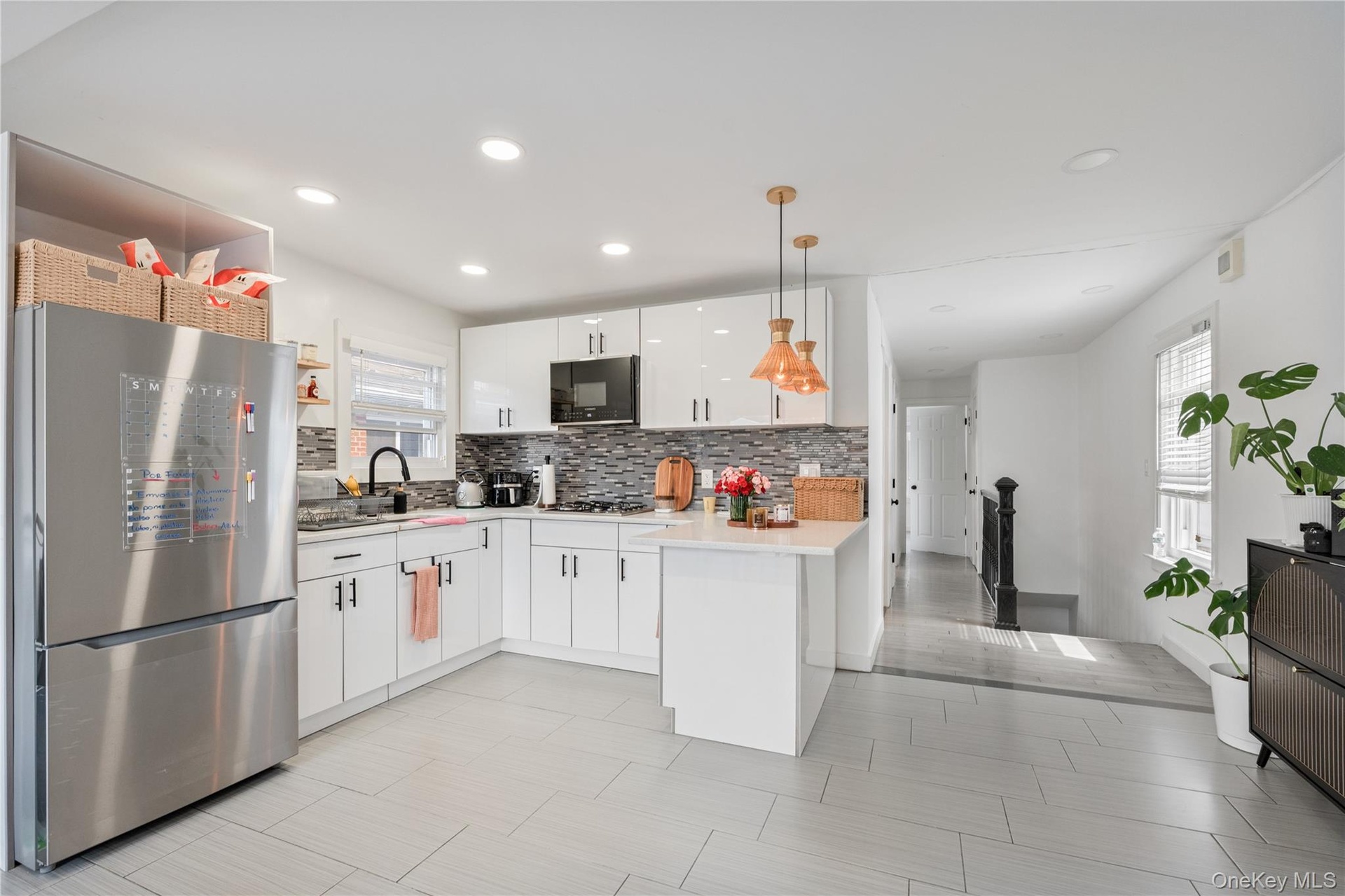 Beautifully updated kitchen featuring modern white cabinetry, stainless steel appliances, tile backsplash, recessed lighting, and a spacious open-conc
