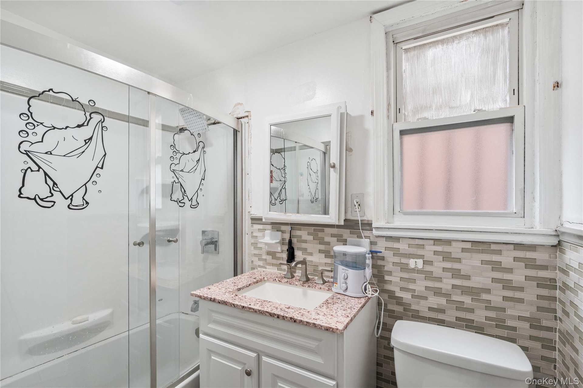 Updated full bathroom featuring a glass-enclosed shower, modern vanity, tile backsplash, and natural light. 1st Floor