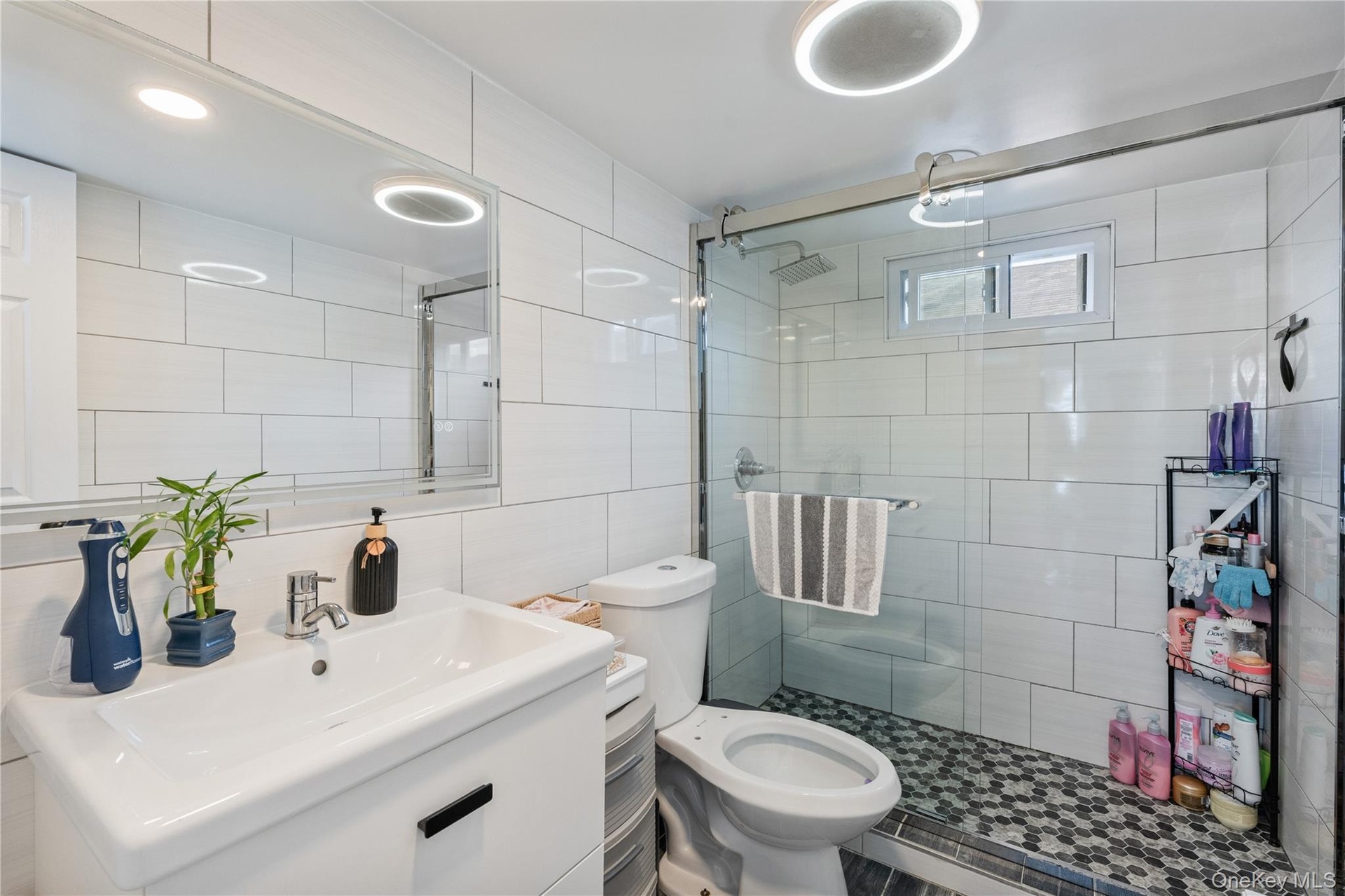 Modern full bathroom featuring a glass-enclosed walk-in shower, contemporary tilework, sleek vanity, and stylish lighting. 2nd Floor Unit.