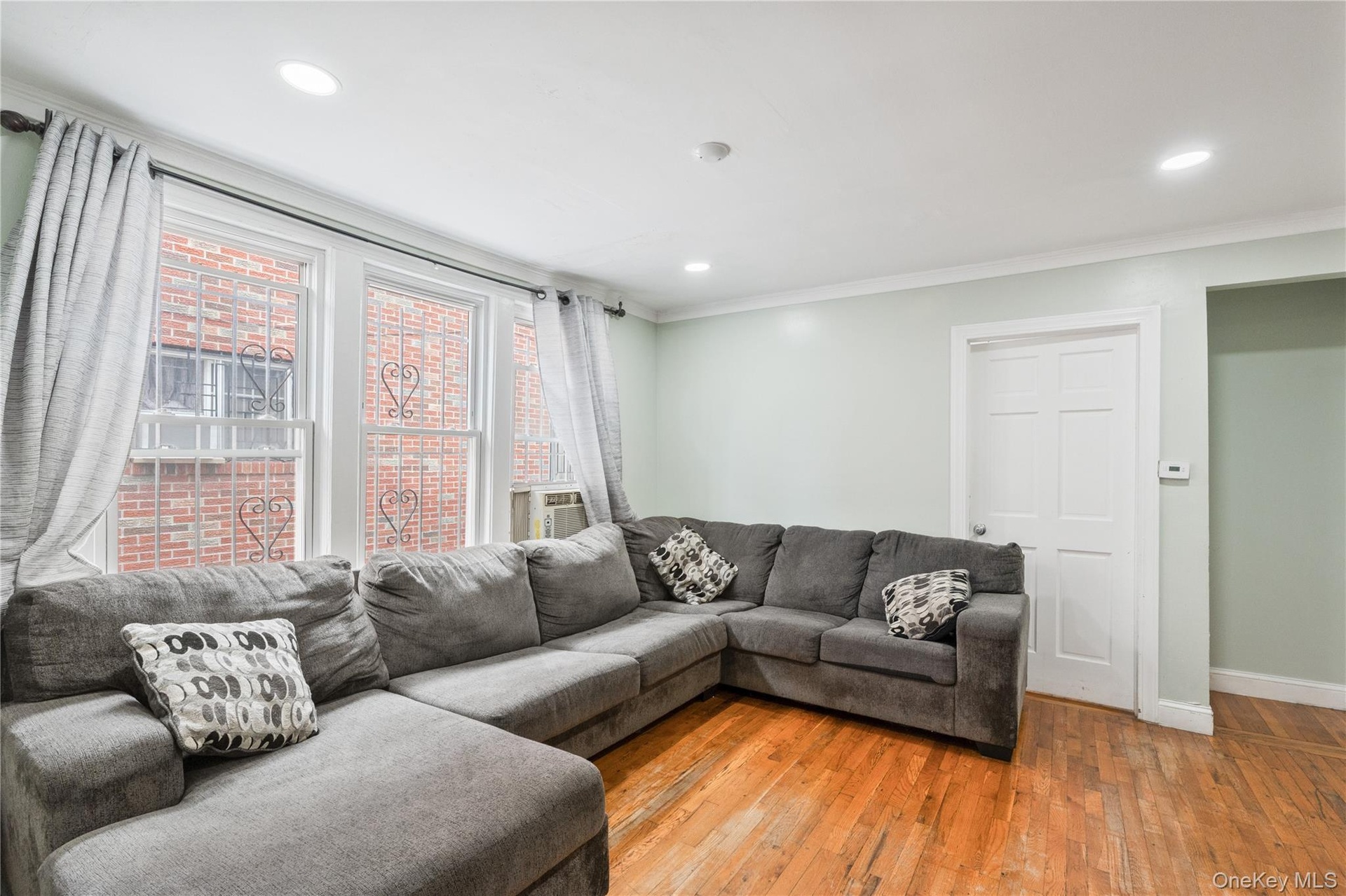 Bright and spacious living room featuring hardwood floors, recessed lighting, and abundant natural light from multiple windows. 1st Floor.