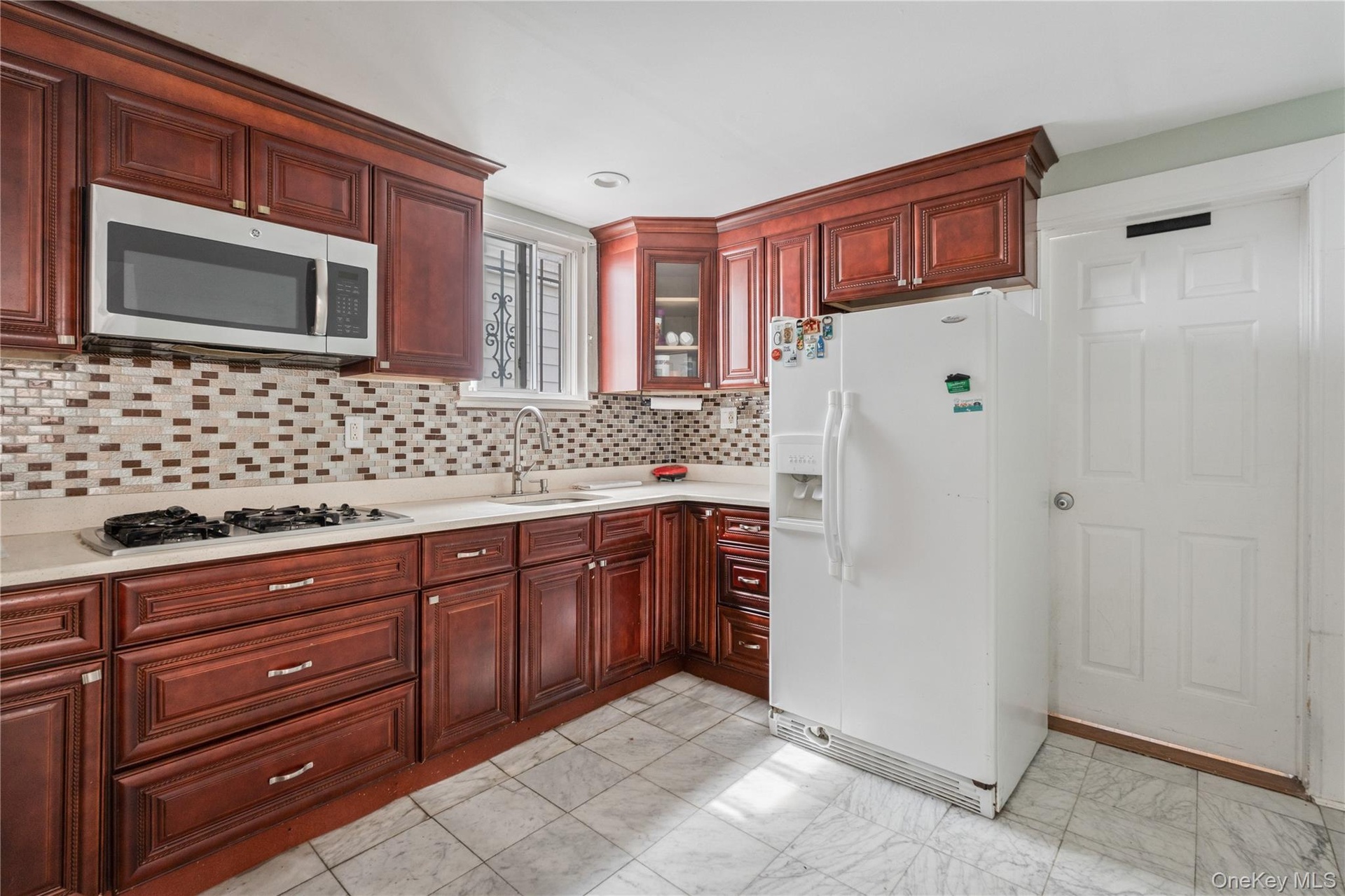Updated kitchen featuring rich wood cabinetry, tile backsplash, ample counter space, and plenty of storage. 1st Floor.