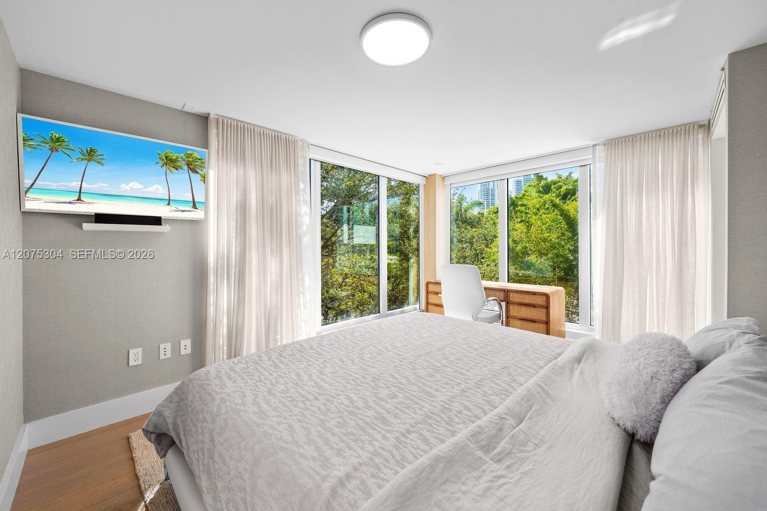 Primary bedroom with large windows, wood floors, and serene ambiance — bright retreat in South of Fifth neighborhood.