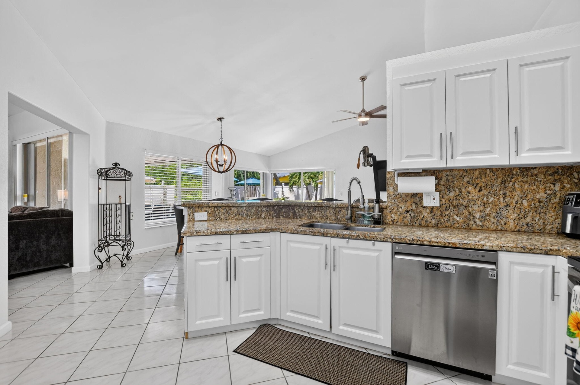 Bright, open kitchen featuring white cabinetry, granite countertops, stainless steel appliances including a dishwasher, pendant lighting, ceiling fan,