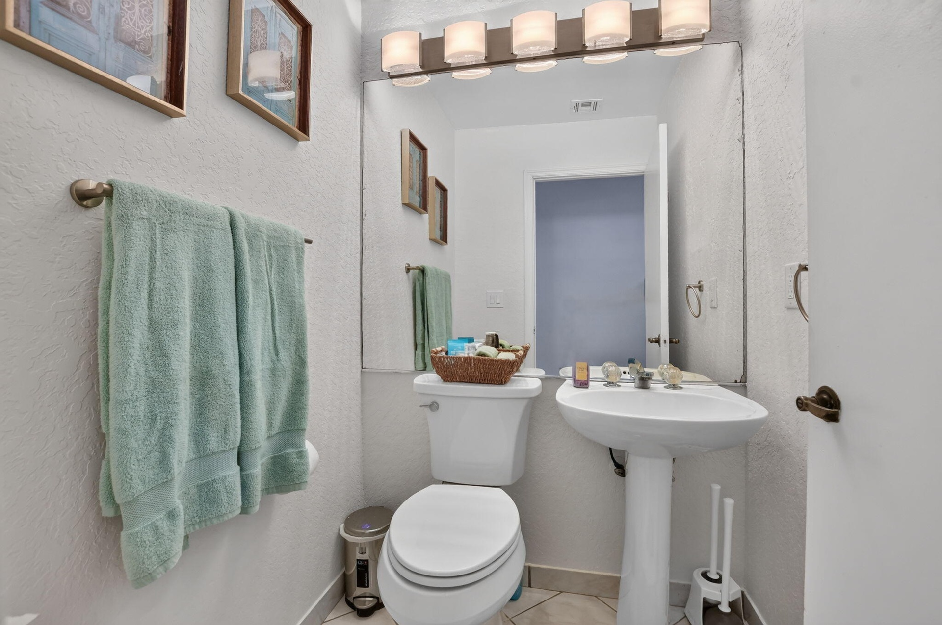 Pedestal sink with a single-handle faucet, wall-mounted mirror, and vanity lighting fixture