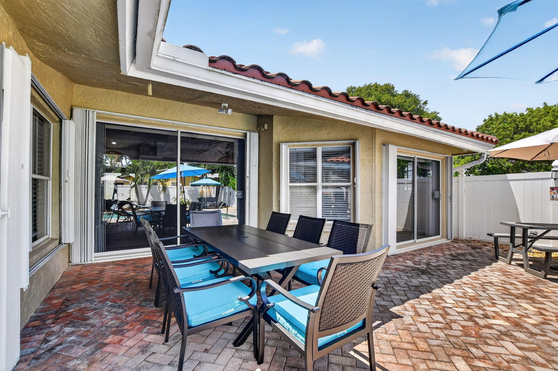 Exterior patio with brick-finish pavers, sliding glass doors, white-framed windows, and a terracotta tile roof