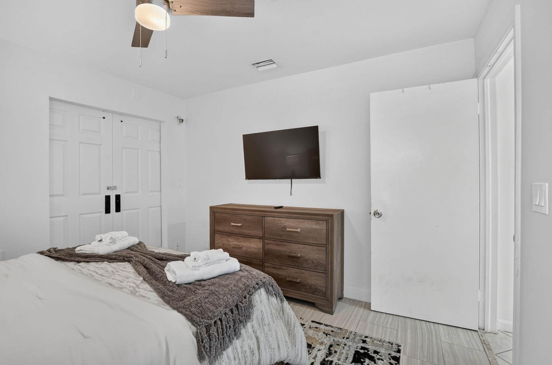 White walls, bi-fold closet doors, wood-finish flooring, and a ceiling fan with light fixture
