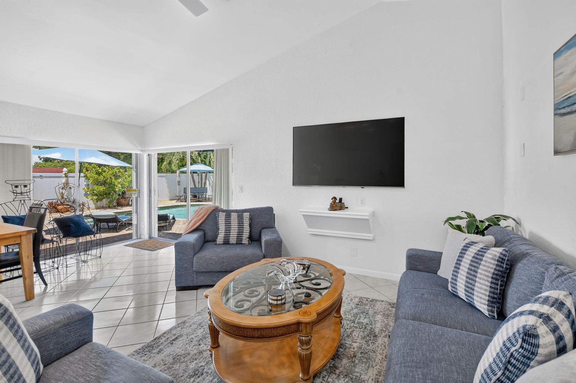 Vaulted ceiling, white tile flooring, ceiling fan, sliding glass doors, and a swimming pool