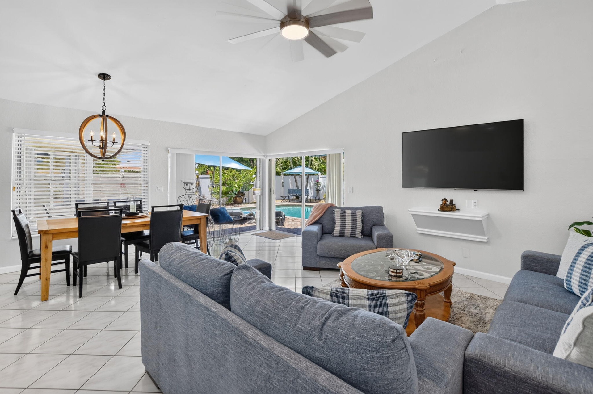 Vaulted ceilings with a ceiling fan, white tile flooring, sliding glass doors to the exterior, and a dining area with a chandelier