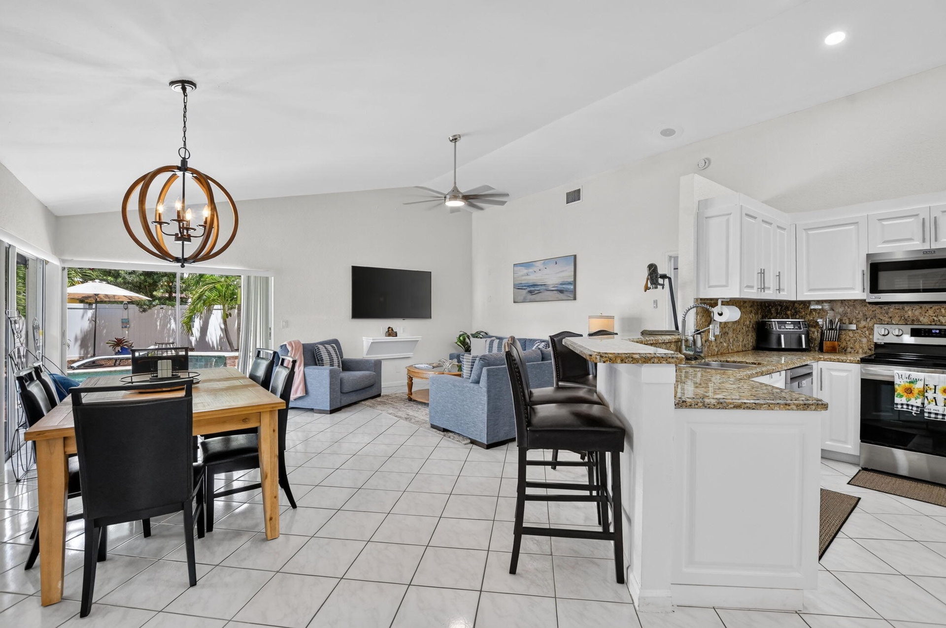 Open-concept living and kitchen area featuring light-filled spaces with large glass sliding doors, white cabinetry with granite countertops, stainless