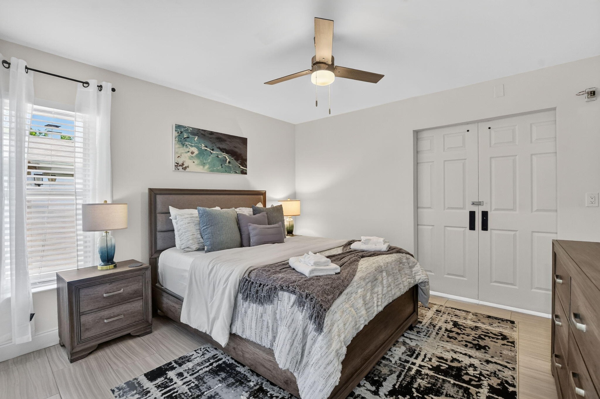 Light wood-finish flooring, two-panel bifold doors, window with blinds, and a ceiling fan with integrated lighting