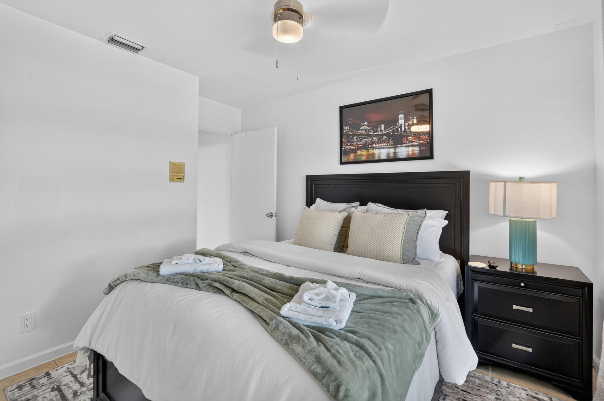 Recessed lighting, wood-finish flooring, ceiling fan, dark wood headboard, and bedside table with storage