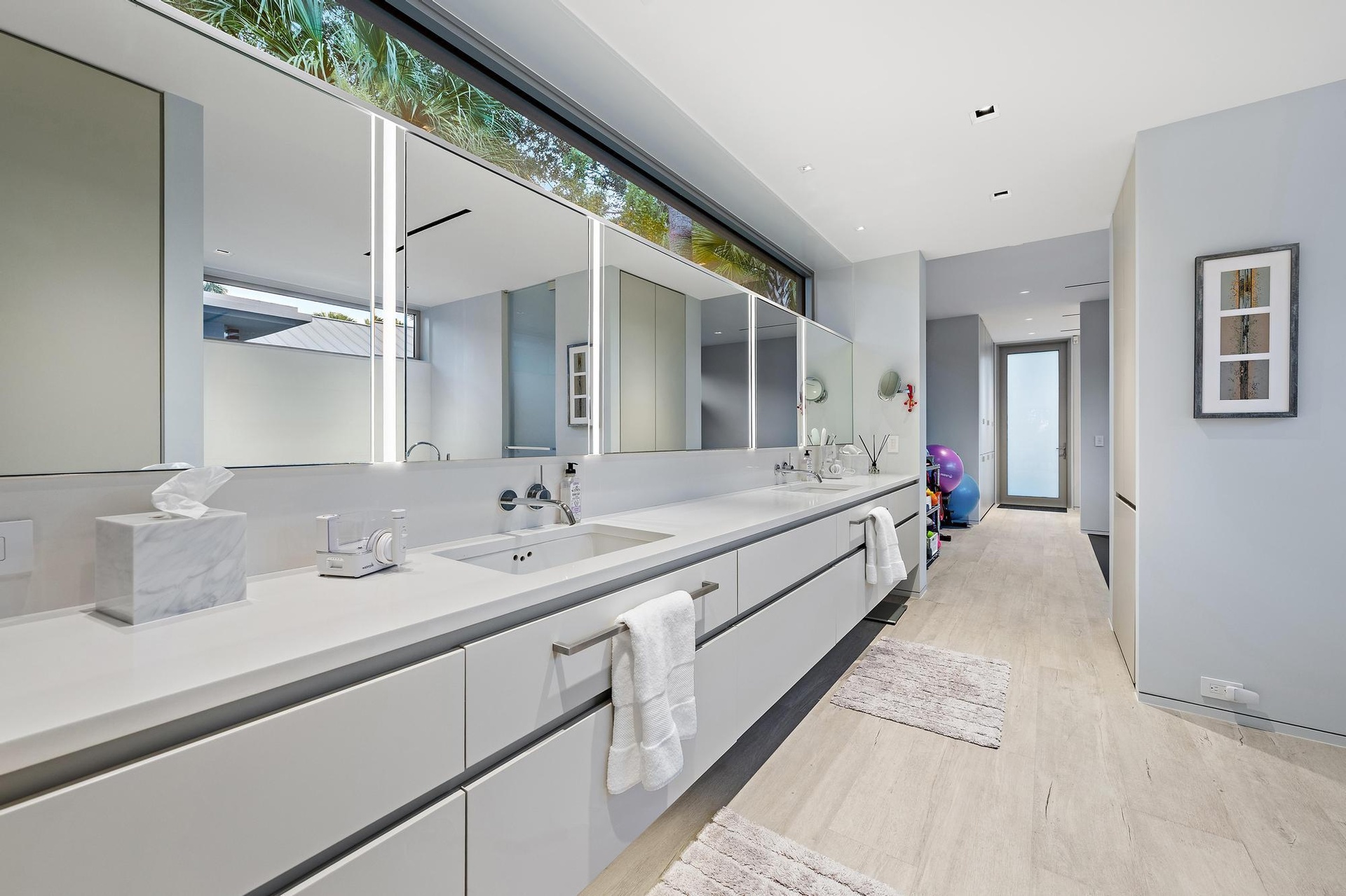 Dual vanity with integrated sinks, white countertops, built-in medicine cabinets with integrated lighting, wood-finish flooring, and a large horizonta