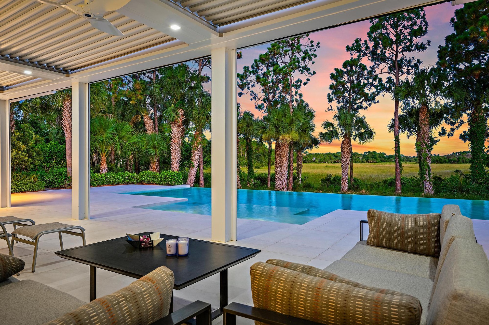 Covered outdoor living space featuring an infinity-edge pool, large format patio pavers, recessed lighting, and a ceiling fan