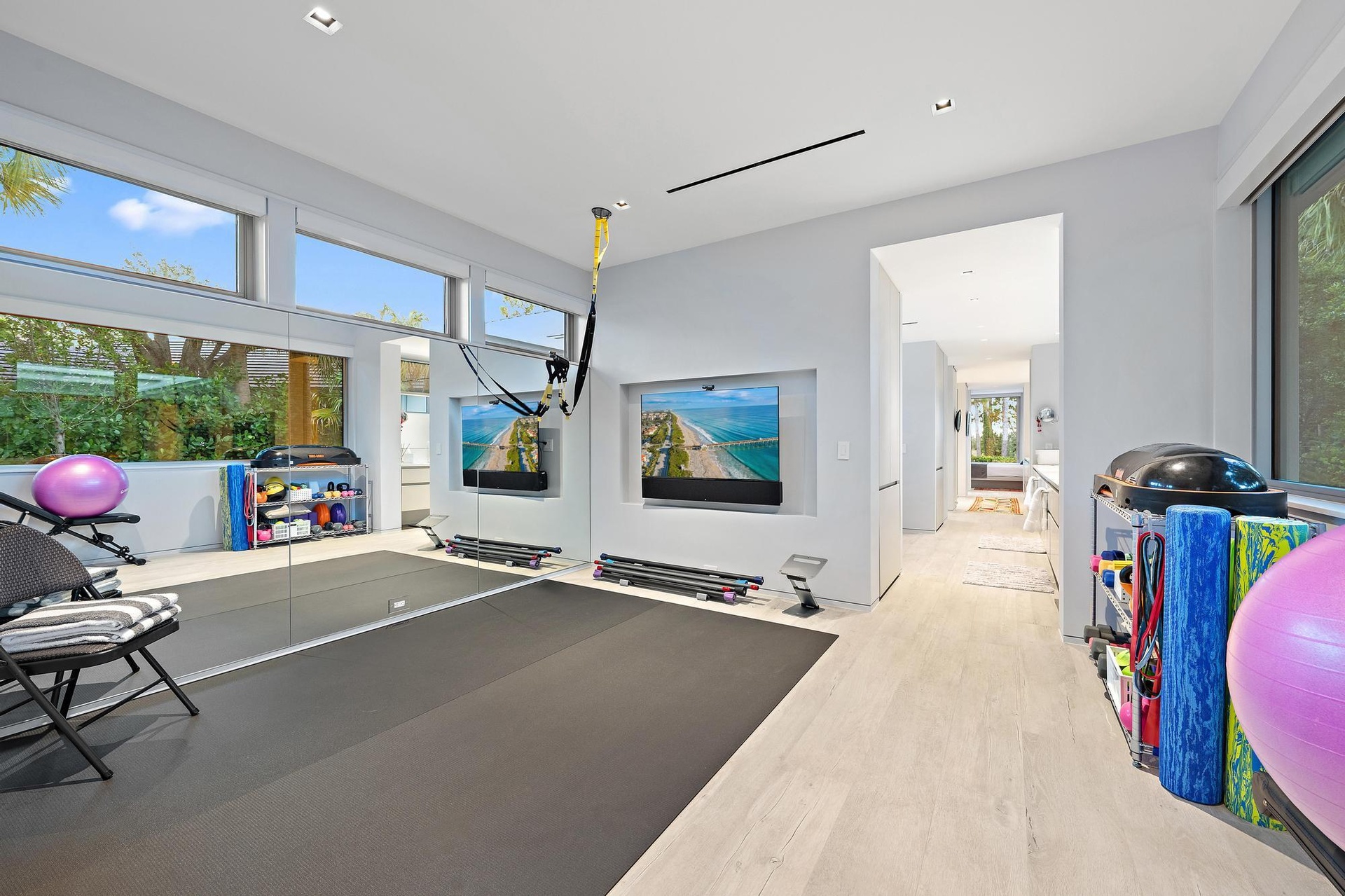 Expansive fitness space featuring light wood-finish flooring, full-height wall mirrors, and large windows with transom panels
