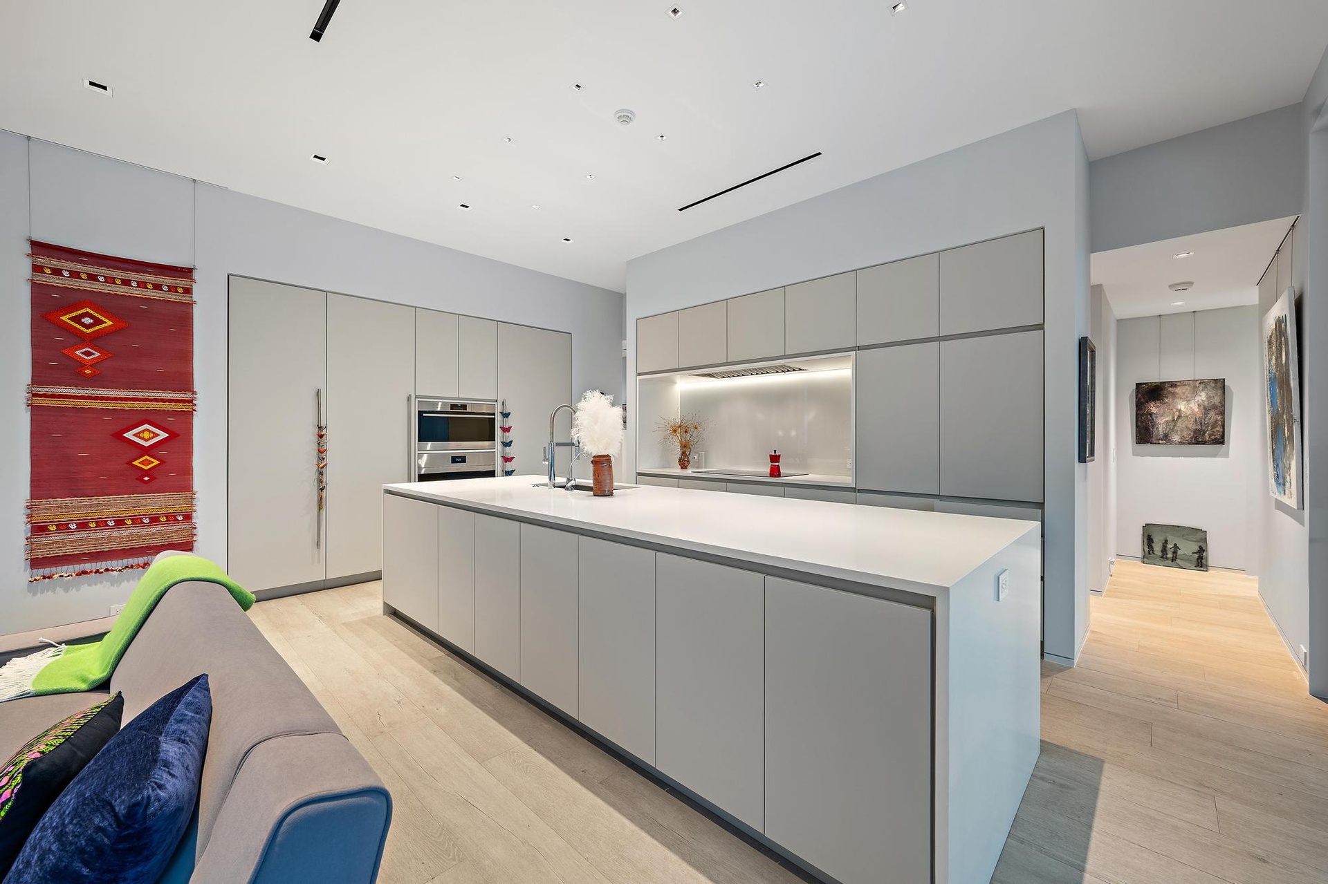 Integrated kitchen featuring a large central island with sink, ample light-grey cabinetry, stainless steel built-in appliances, and light wood-finish 