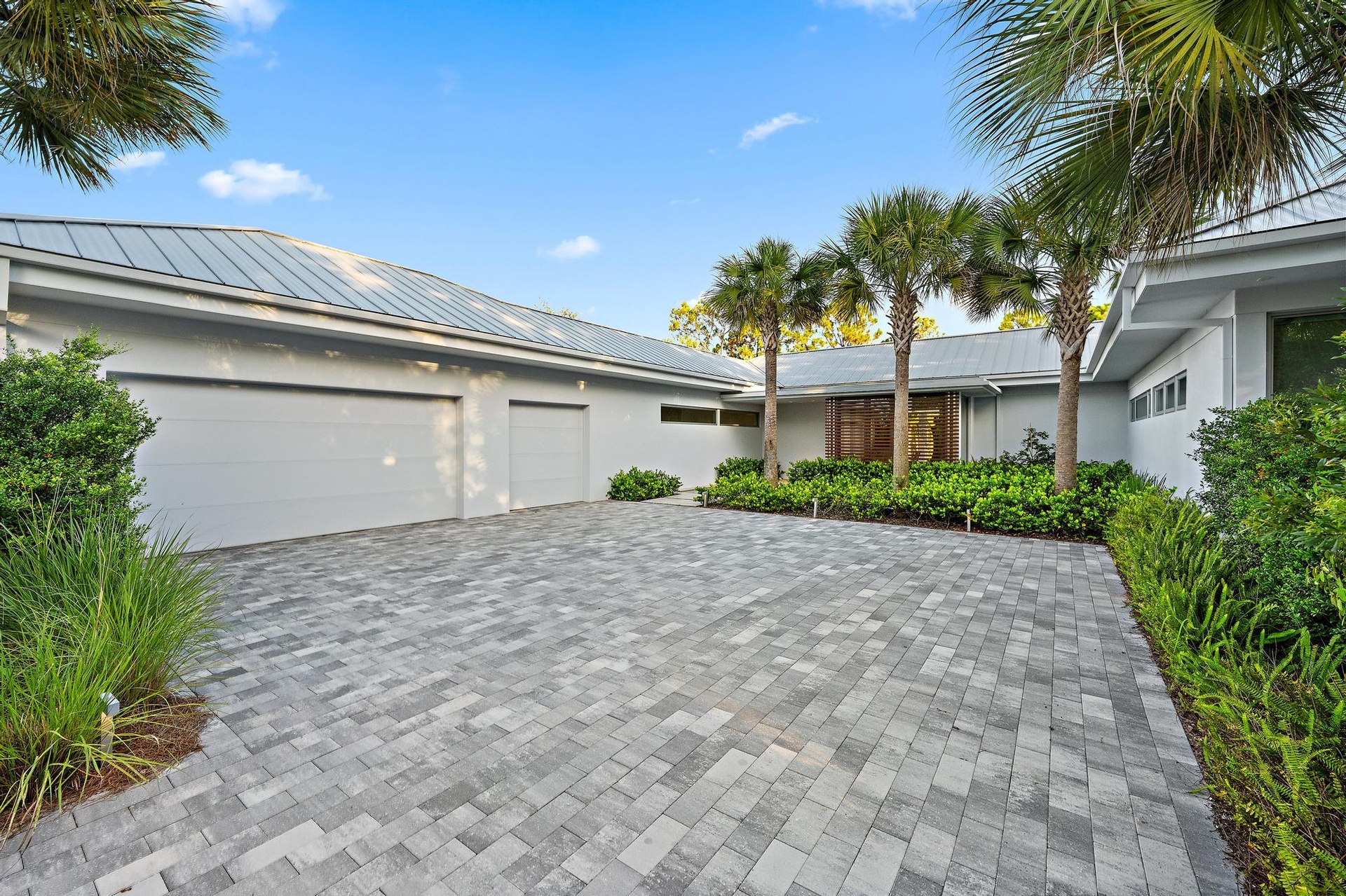 Paver driveway, mature palm trees, contemporary exterior, metal roof, and integrated landscaping